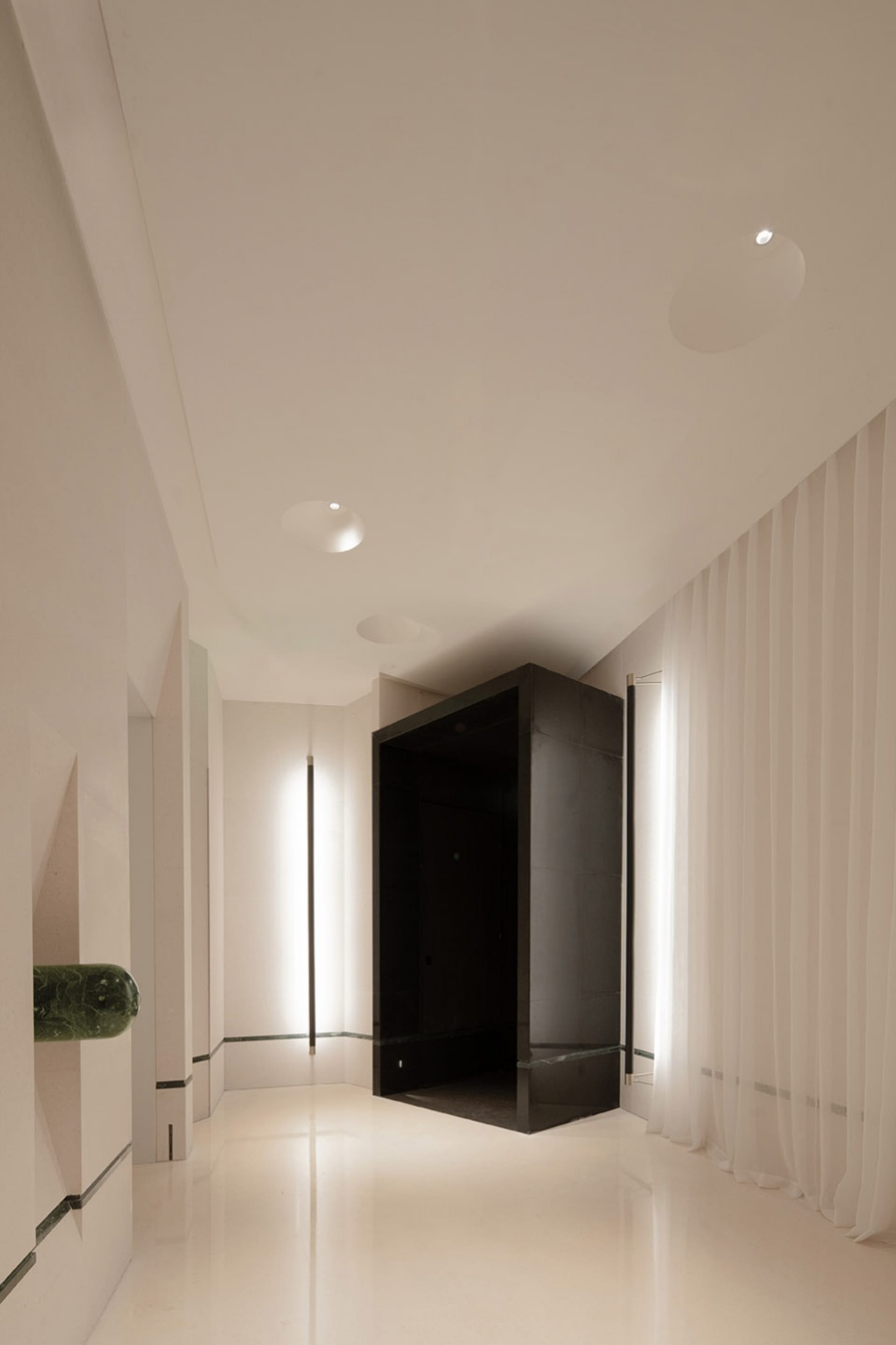 A clean and modern hallway with white walls and floors, lit by overhead lights, creating a calm and quiet atmosphere