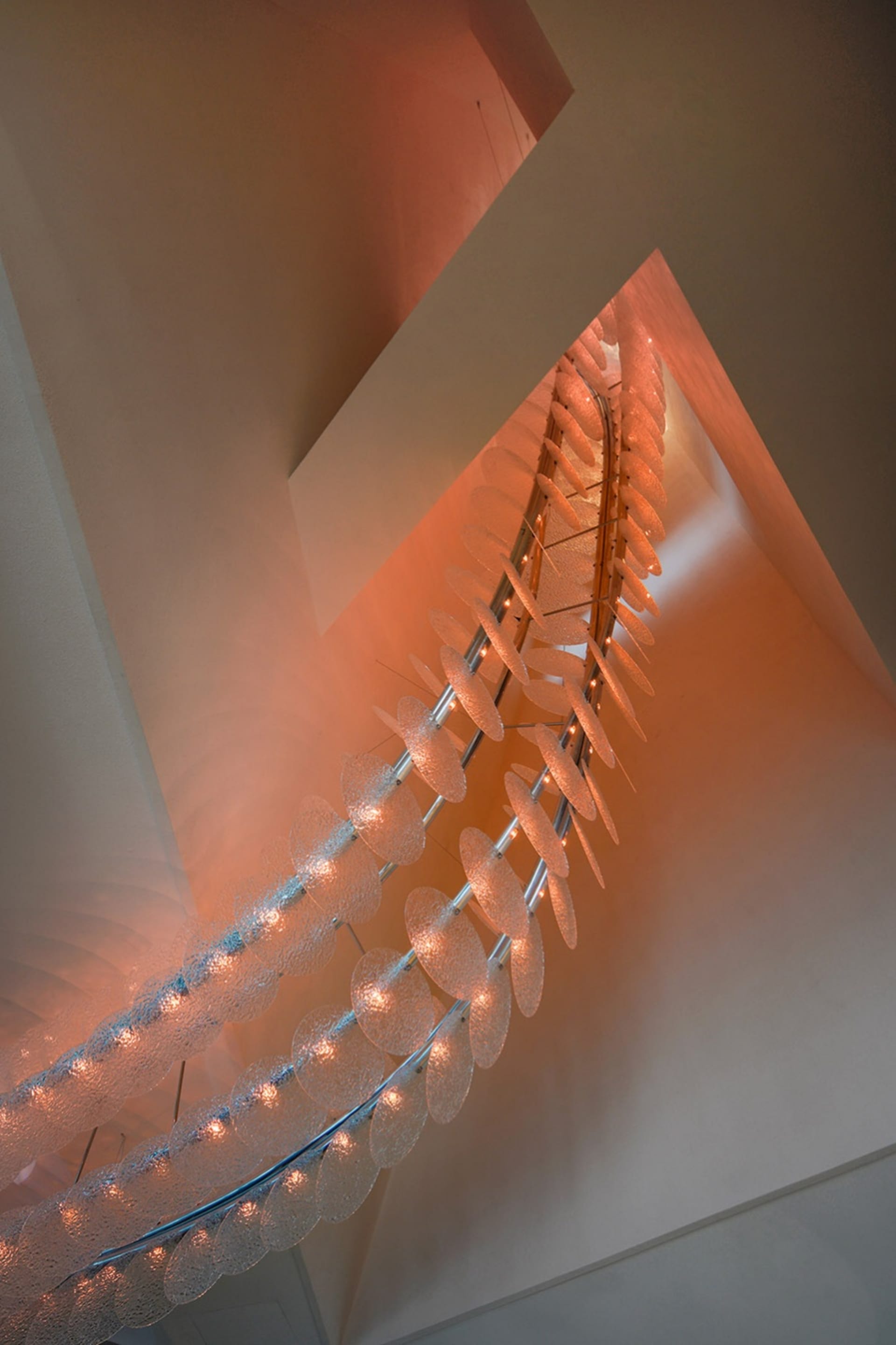 A modern stairwell with a glass chain link fence, illuminated by lights, creating a striking contrast between transparent and opaque elements