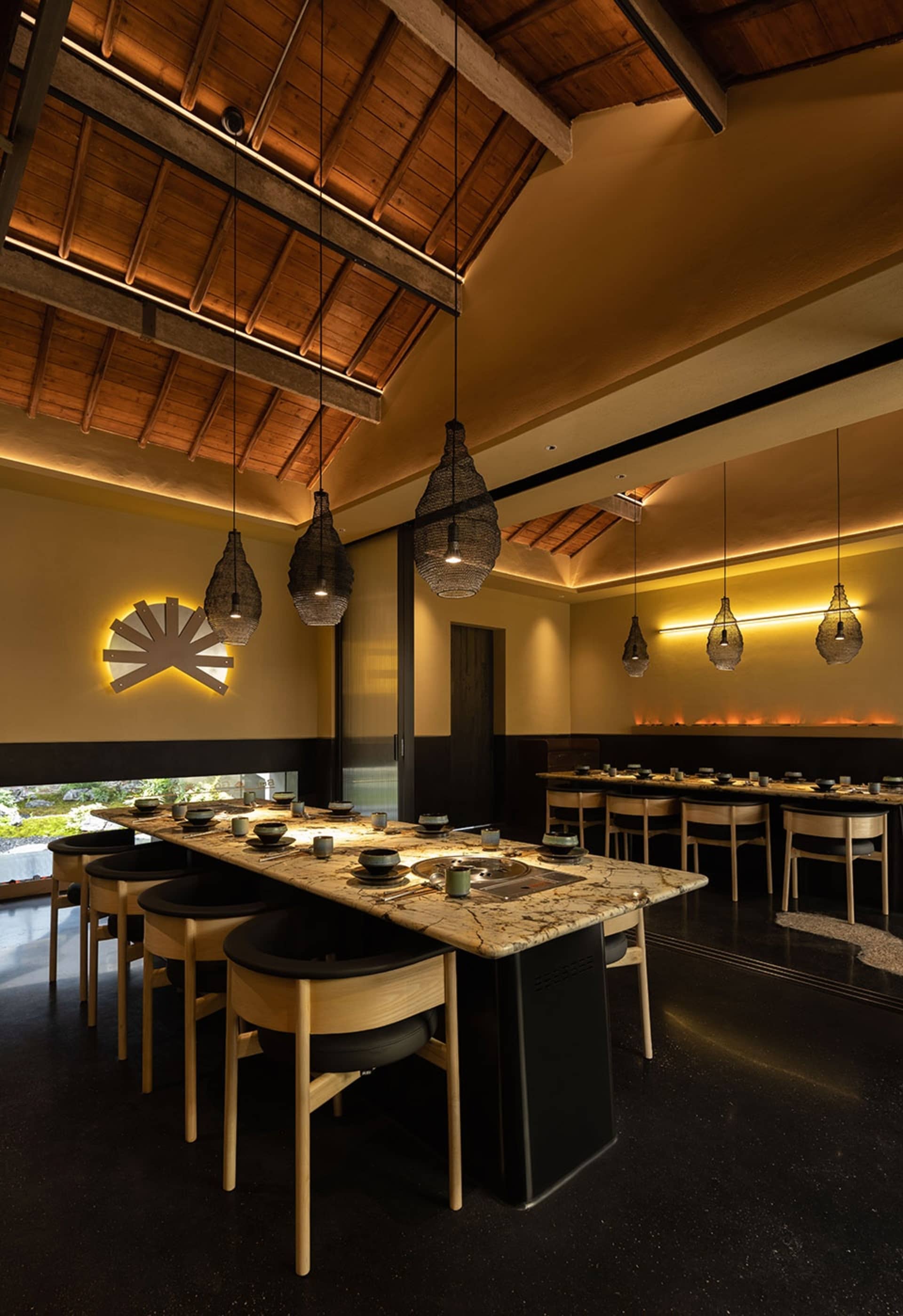 A warm and inviting Asian restaurant interior with a long dining table, chairs, and wooden elements, set for a meal with bowls and cups