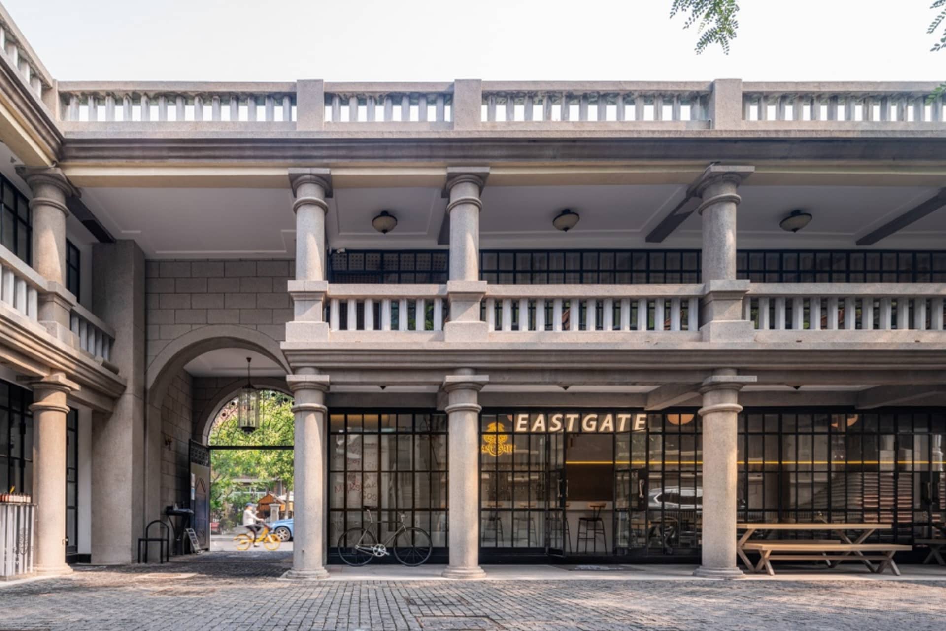 A stone building with a large archway leading to a courtyard where bicycles are parked near a bench, surrounded by a calm and inviting atmosphere