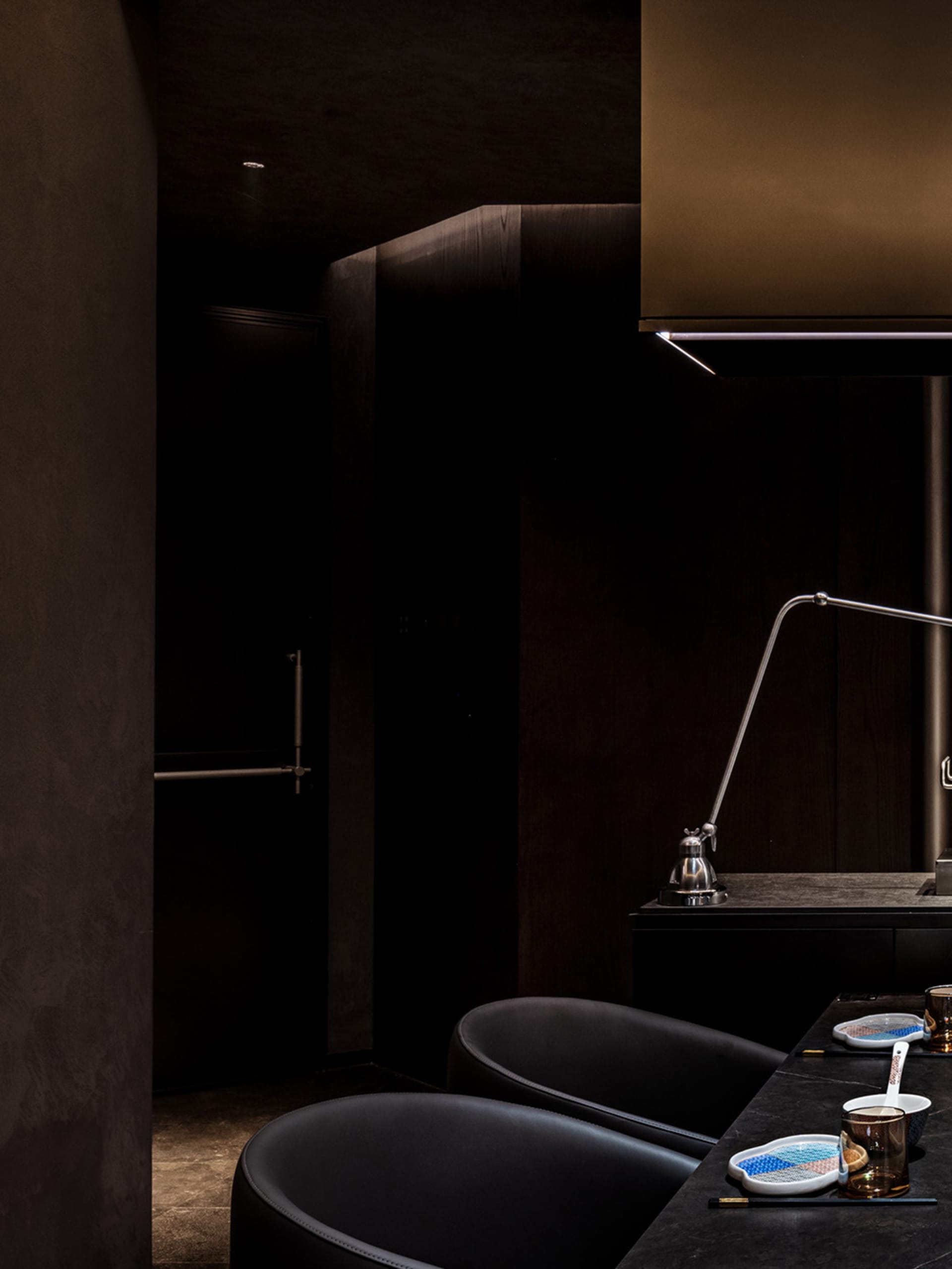 Dark modern kitchen with black cabinets, a sink area, oven, and refrigerator, and two chairs for seating
