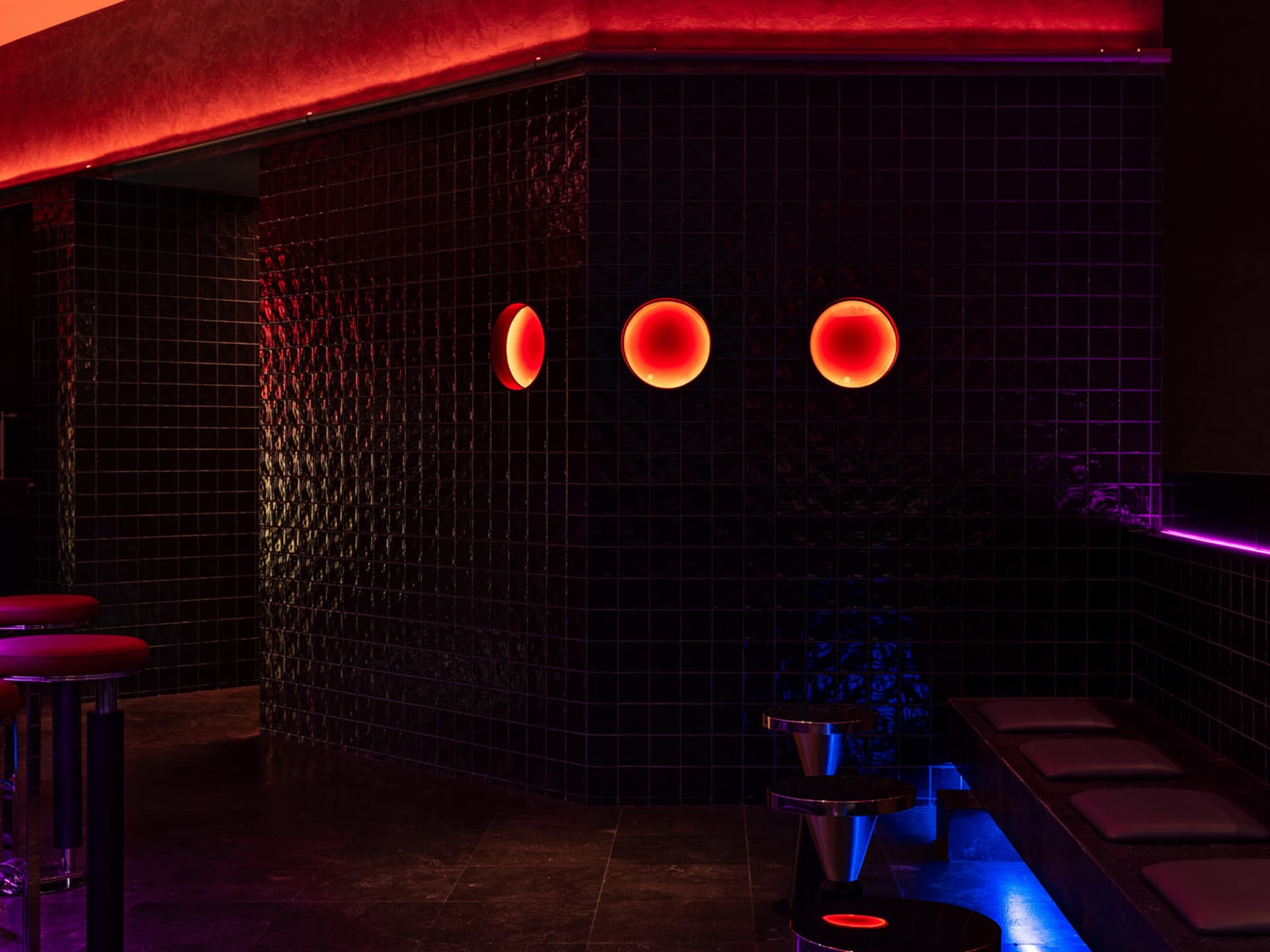 Bathroom with black walls, red accents, three round lights, a sink, and a bench, giving off a modern and sleek vibe