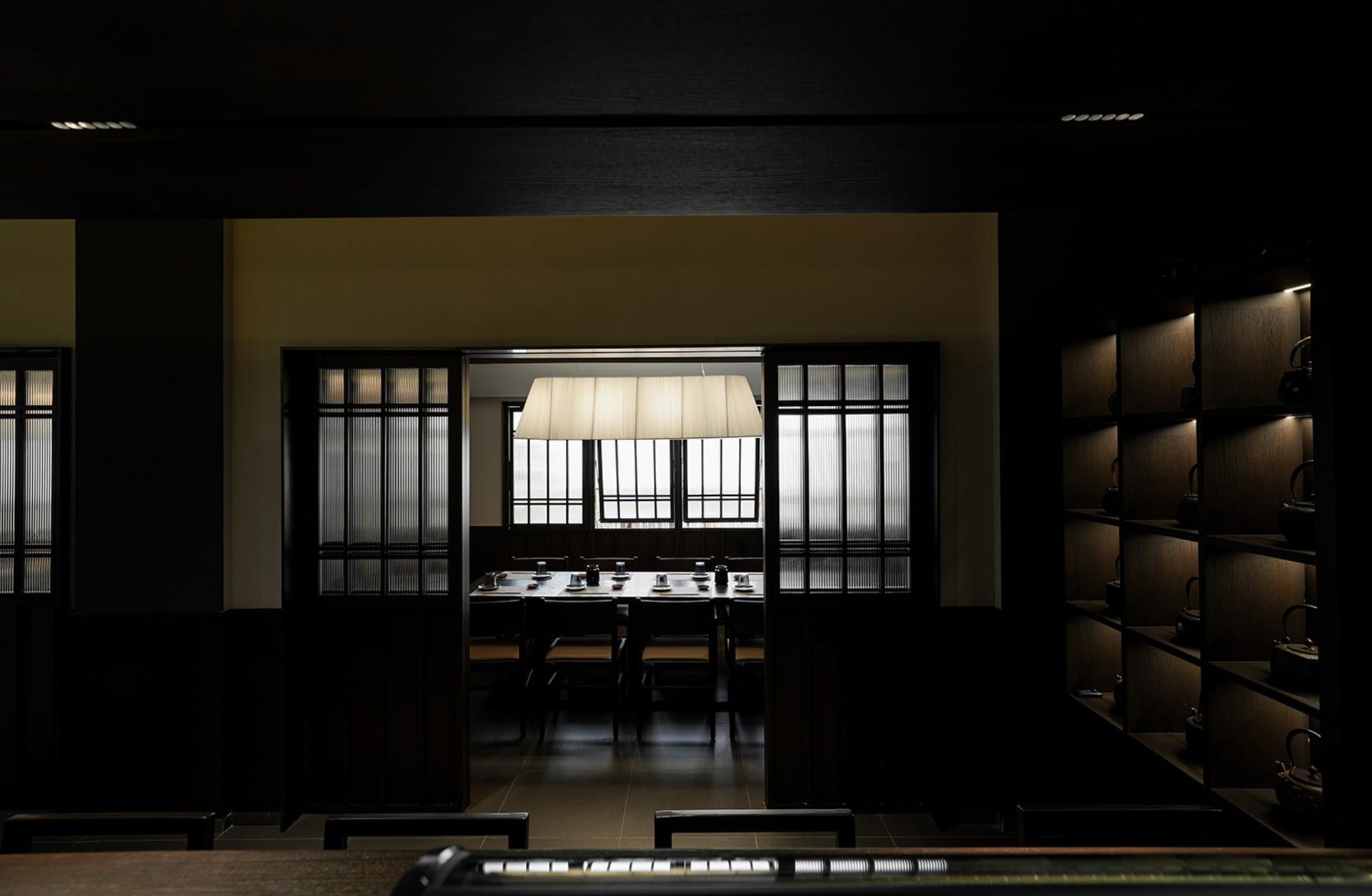 Dark dining space with wooden floors and walls, featuring chairs and tables arranged in a restaurant setting