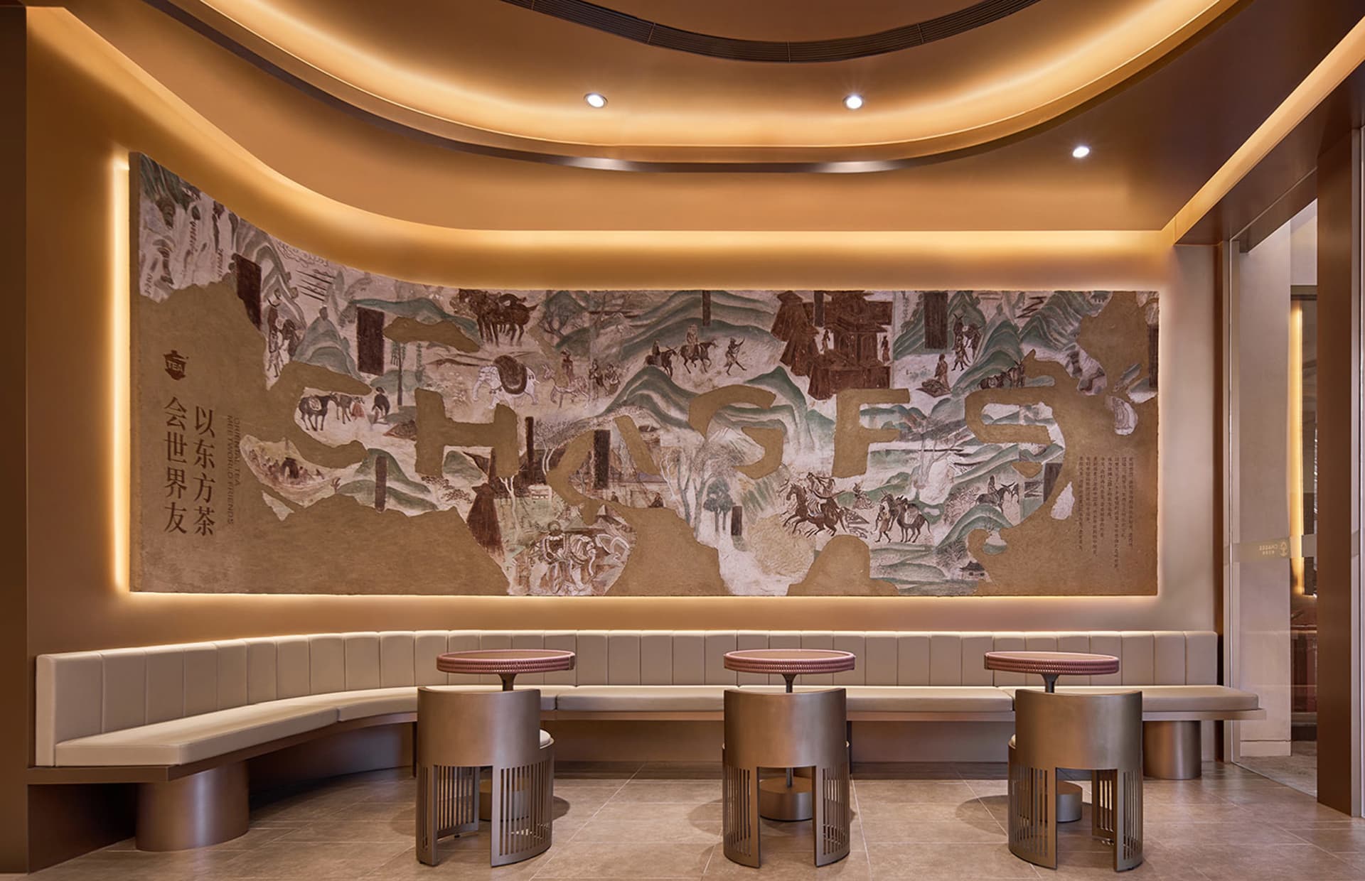 A restaurant interior with a large wall painting of a map featuring people, horses, trees, and buildings, surrounded by chairs and two dining tables, giving off a warm and inviting atmosphere