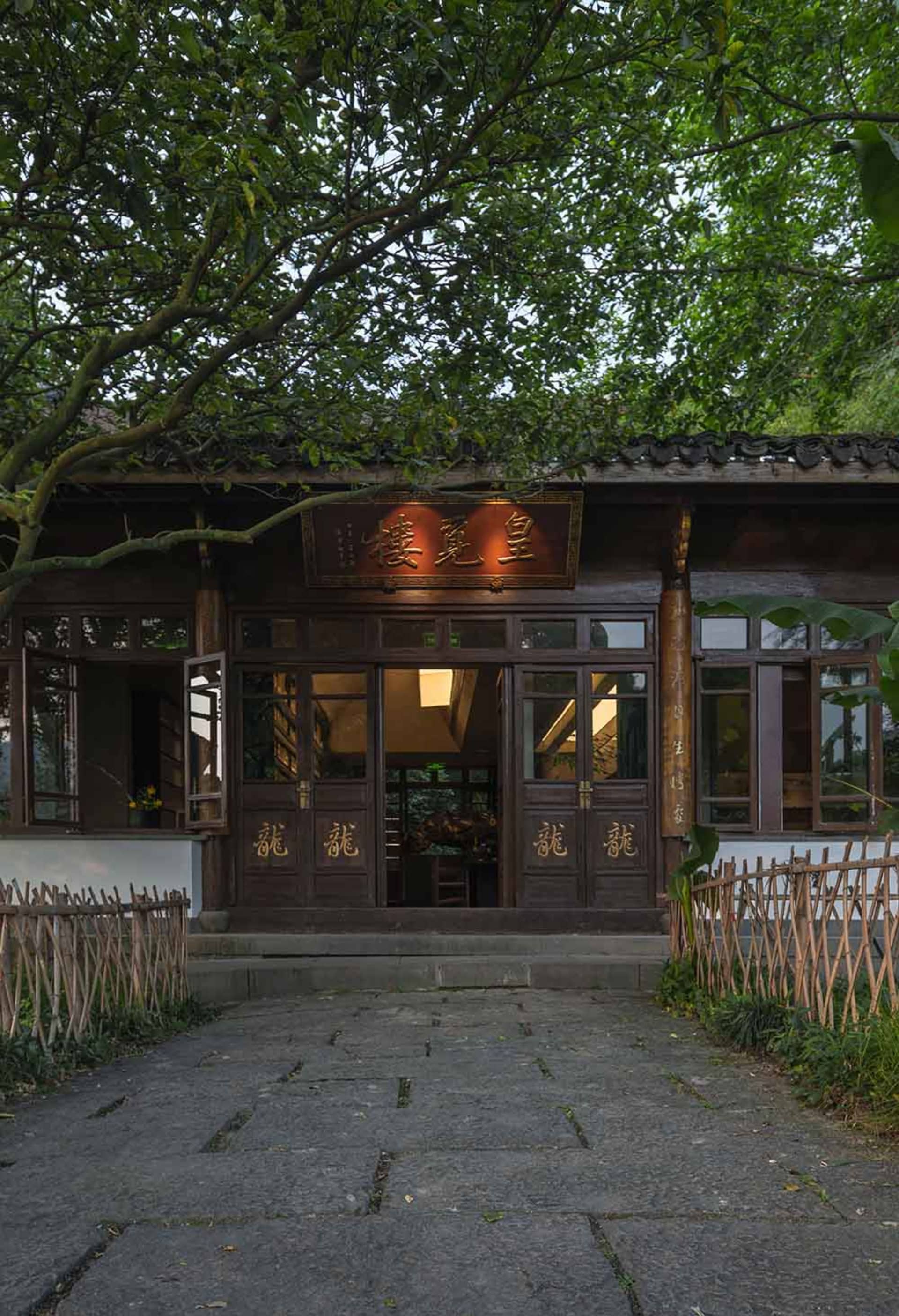 Asian-style house with wooden walls, stone walkway, balcony, and potted plants, set in a calm and serene environment