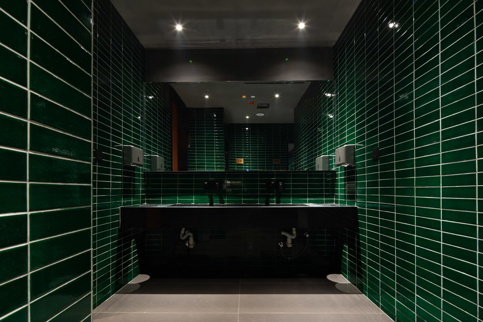 Bathroom with green tiles on the walls, black marble countertops, and two sinks, giving a clean and well-maintained atmosphere