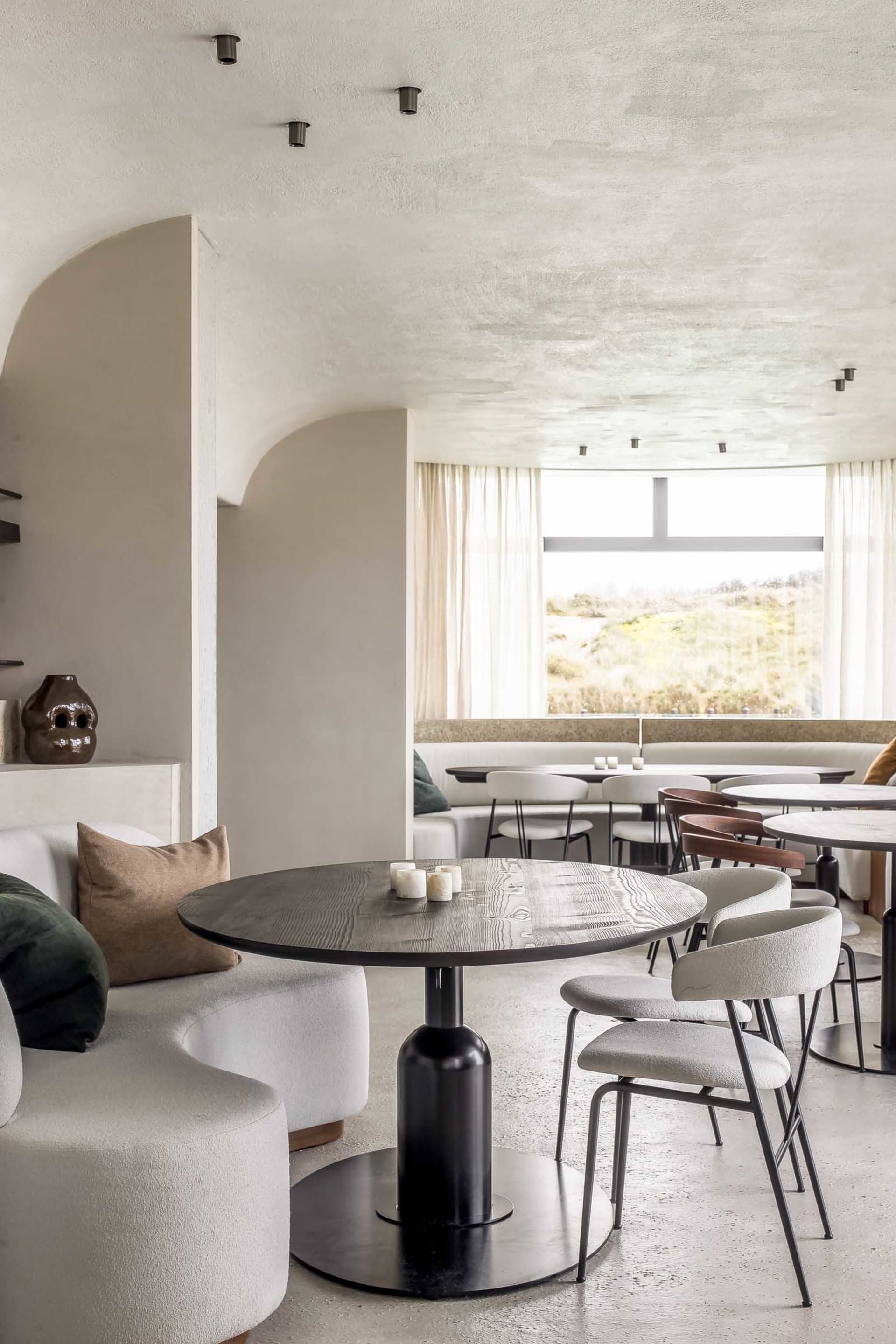 Cozy dining area with tables, chairs, couches, potted plants, and a mix of wood and metal materials in a modern and stylish setting