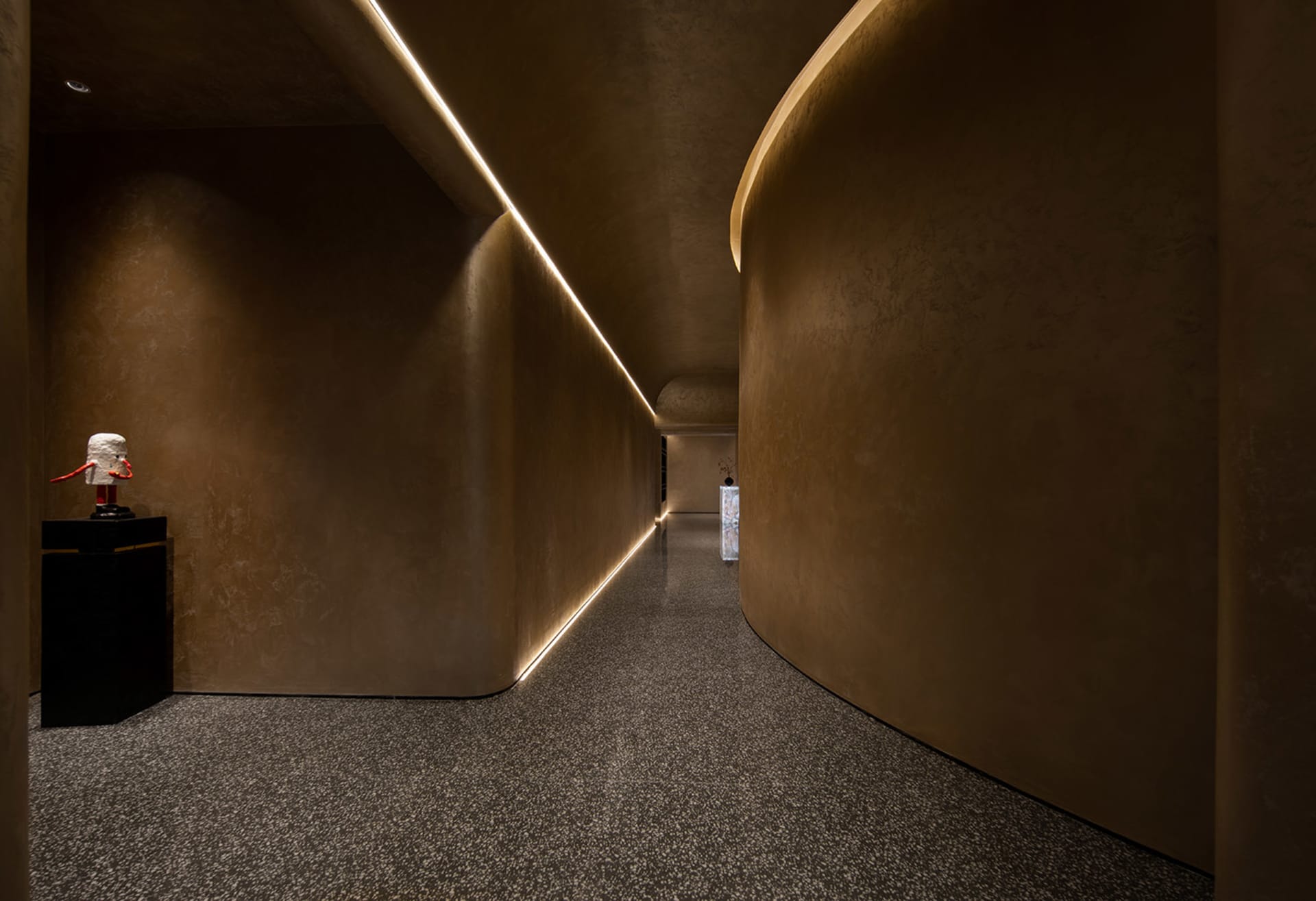 A long, curved hallway with a brown color scheme, lit by lights on both sides and featuring a person standing in the center