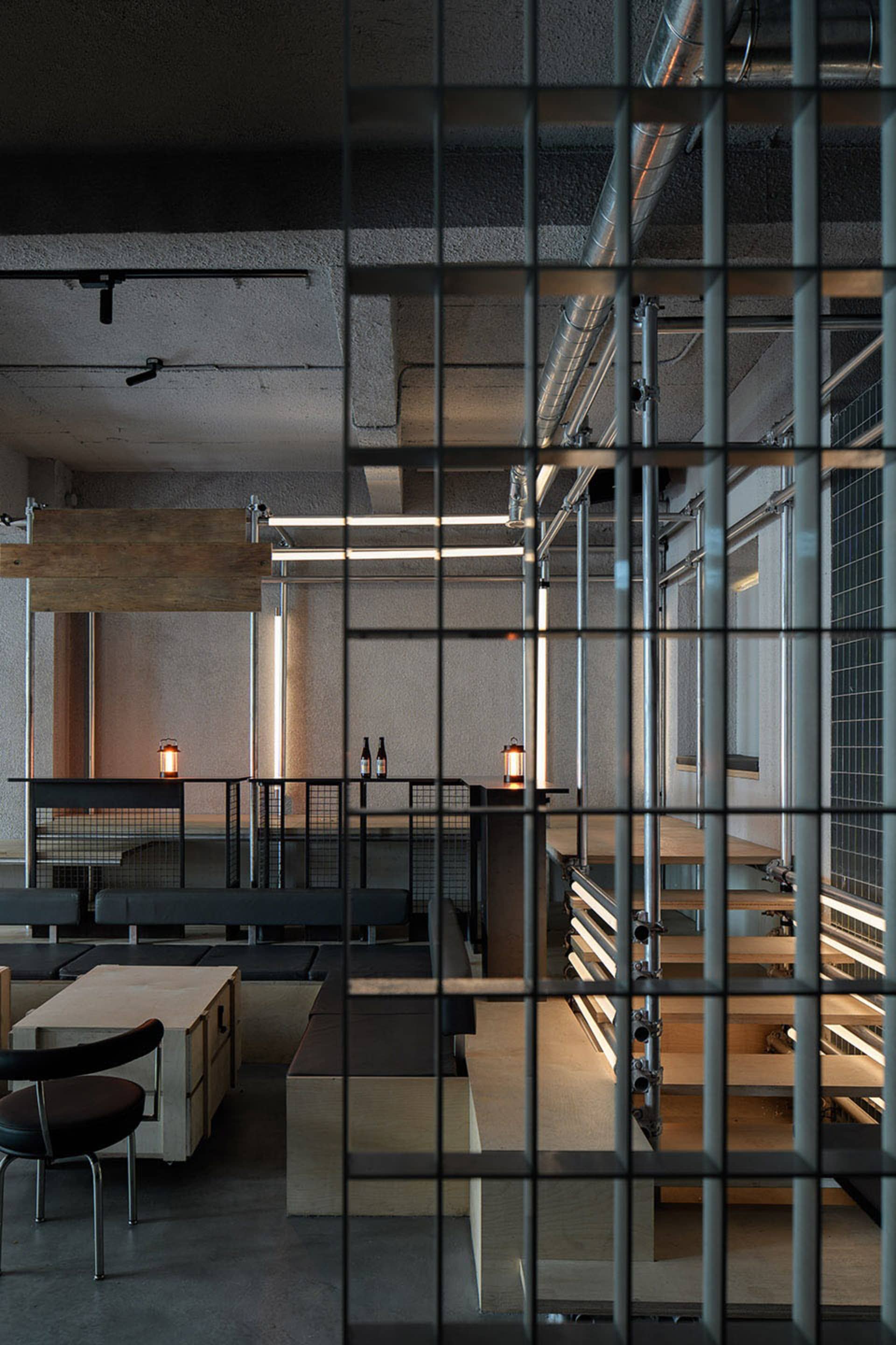 Industrial kitchen space with a cage-like structure, dining table, chairs, bottles, and vases in a dark and moody atmosphere