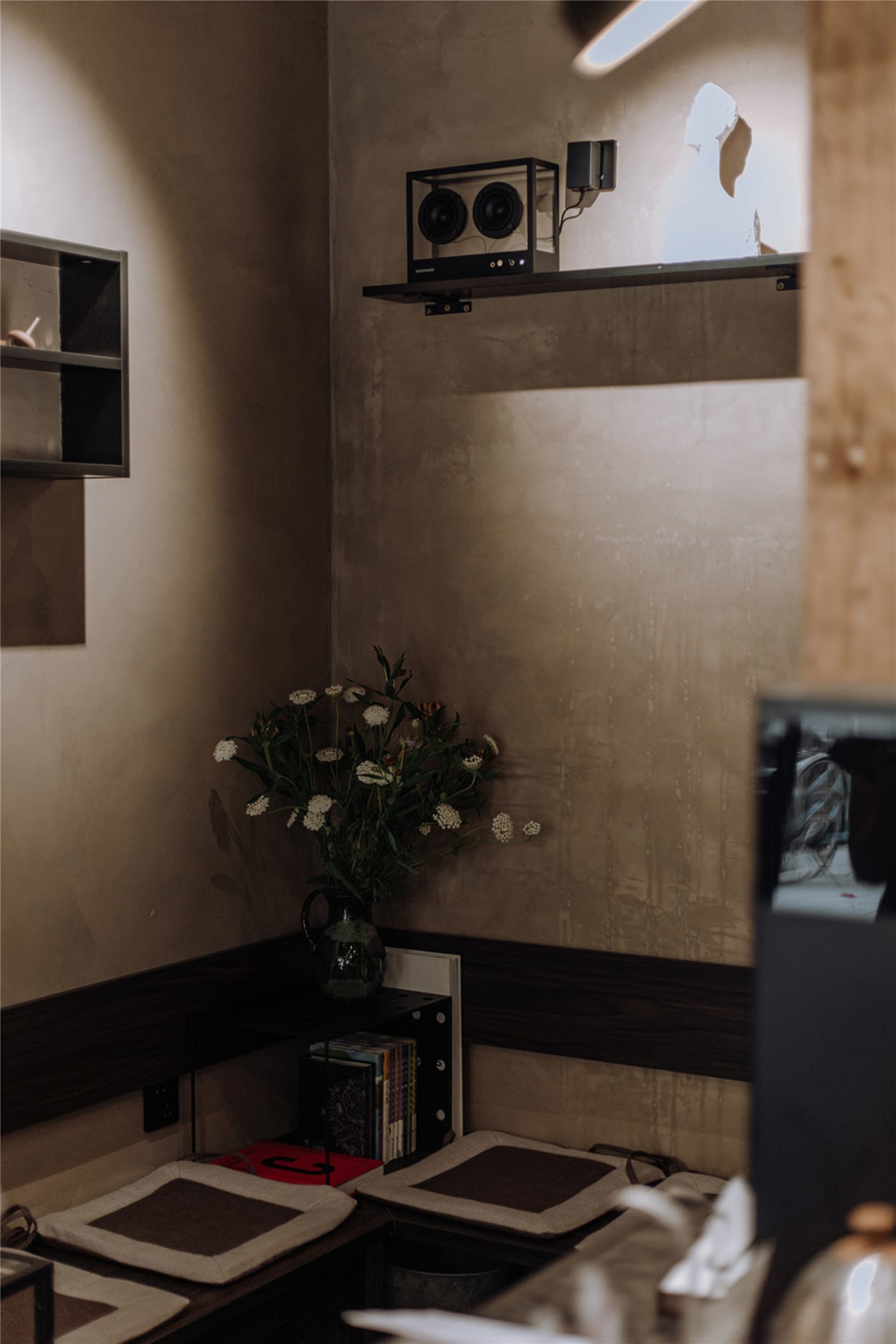 A dimly lit room with a vase of flowers on a table, two speakers, and a TV mounted on the wall, in a minimalist style with a focus on functionality and simplicity