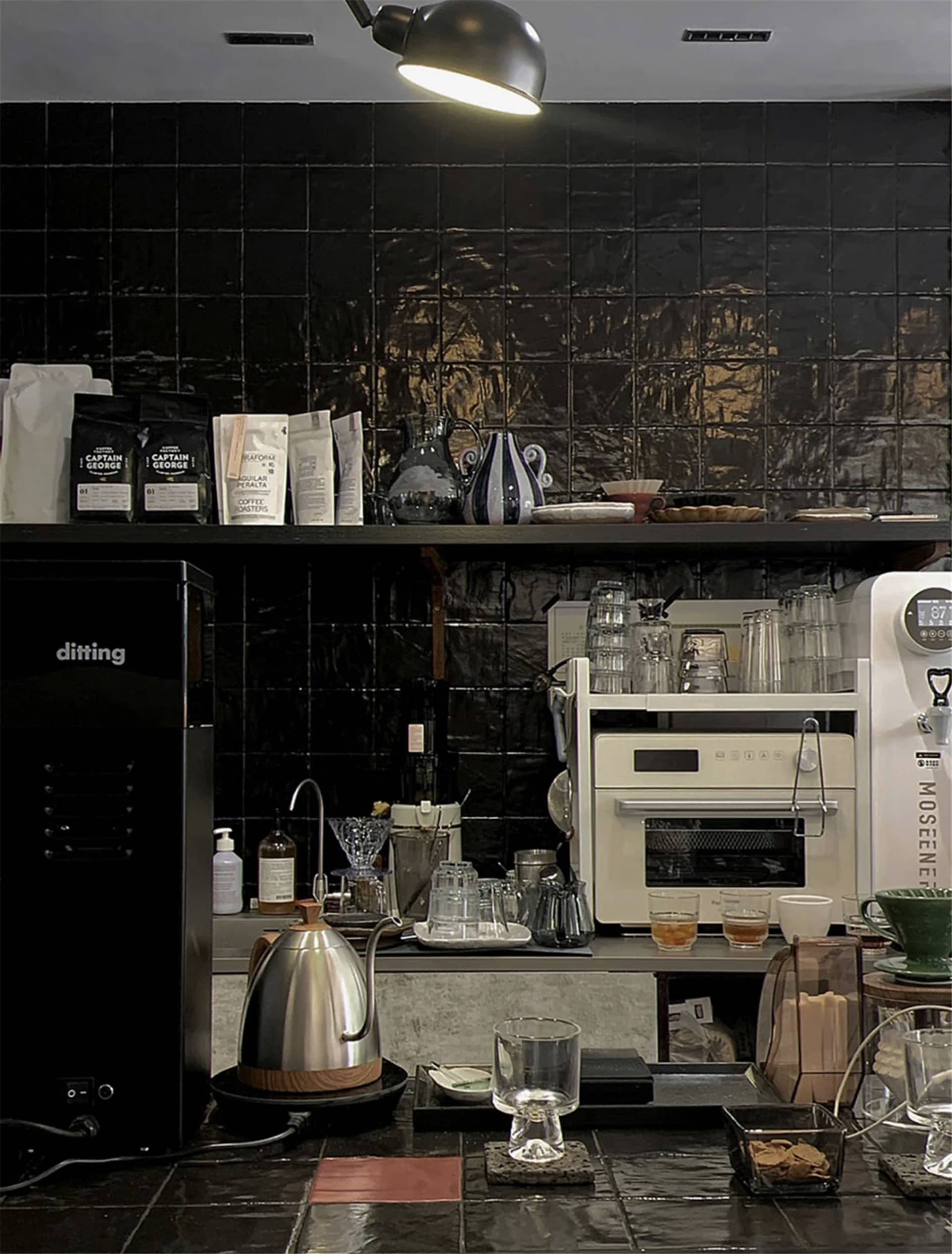 A modern kitchen with a black tile backsplash, two refrigerators, an oven, microwave, and sink, with various kitchen items and utensils scattered throughout