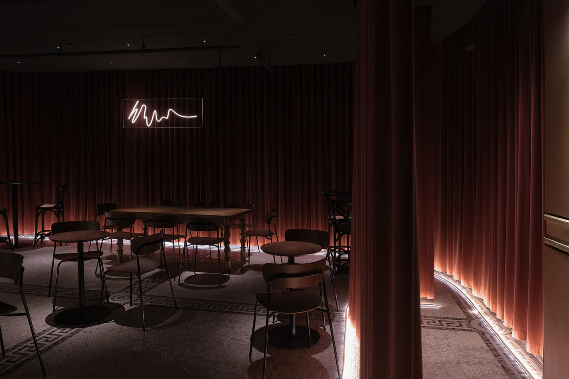 Dimly lit dining space with tables and chairs in various positions, featuring brown and orange-toned walls and a warm ambiance