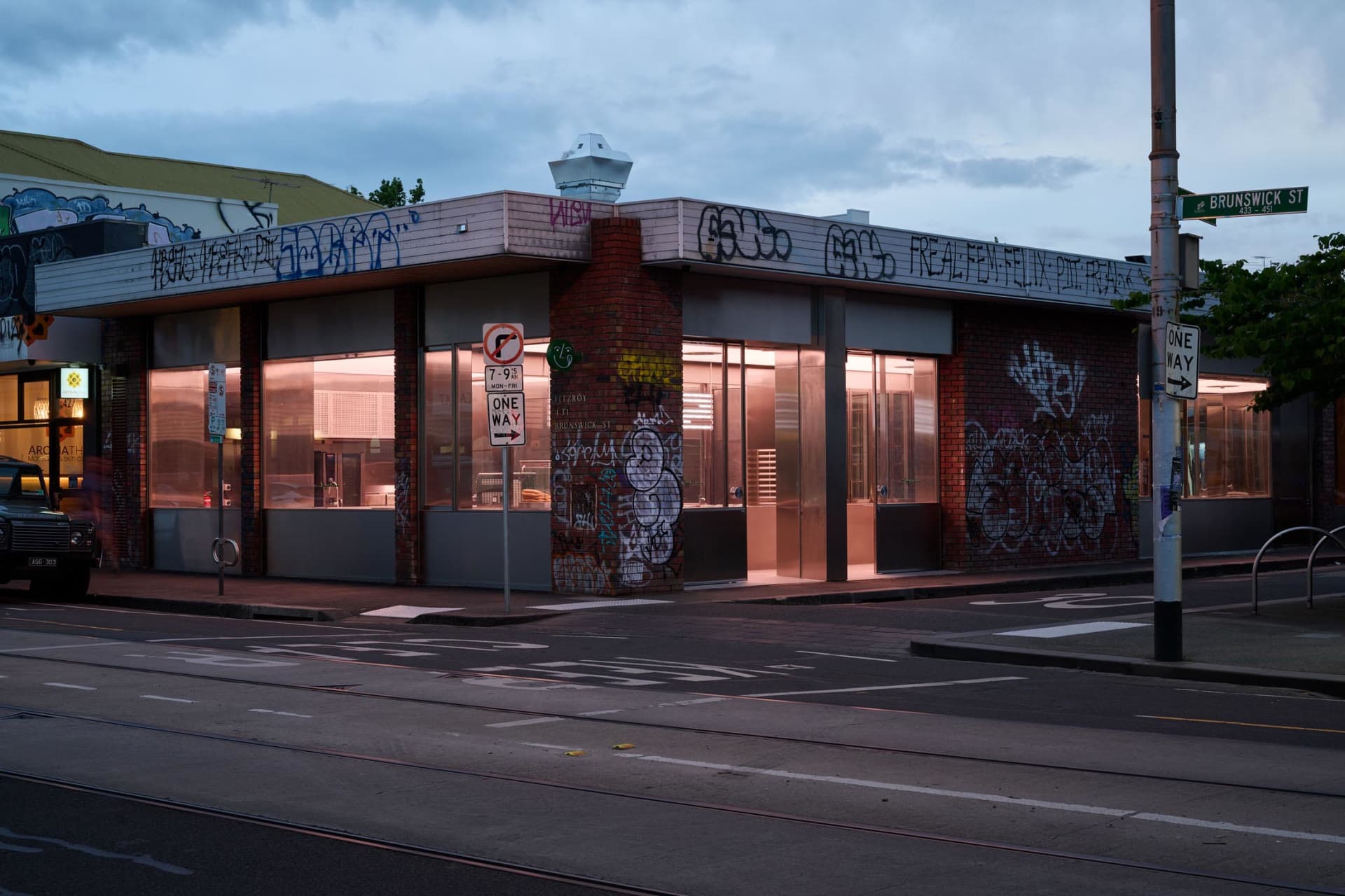 A city street scene with a building featuring graffiti, a no parking sign, and a bicycle parked nearby