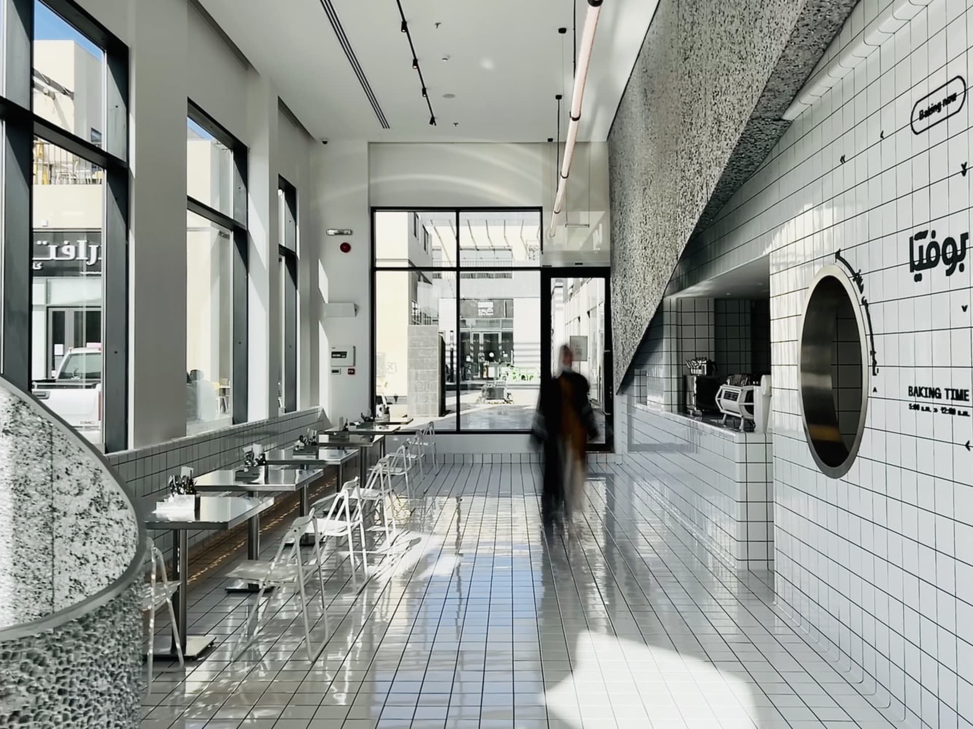A lively restaurant with multiple tables, chairs, and people, featuring a modern and clean atmosphere with tile flooring
