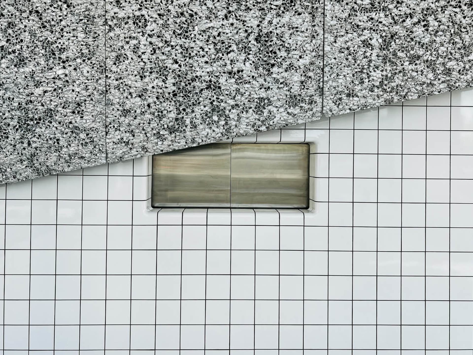 A minimalist interior space with a checkered tiled wall featuring a built-in metal box, creating a geometric and modern look