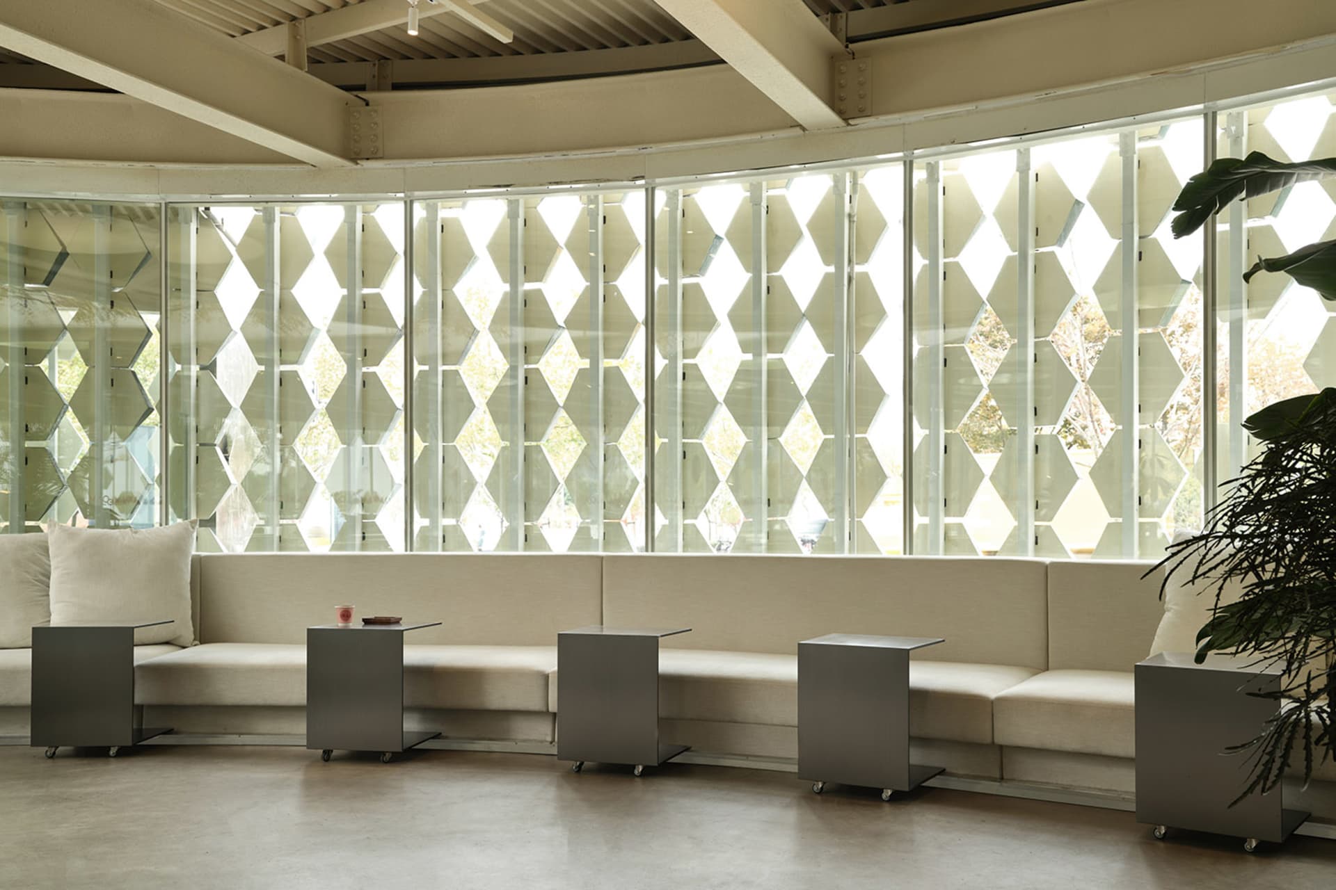 A well-lit interior design featuring a patterned window, benches, dining tables, and a chair, creating a comfortable and inviting atmosphere