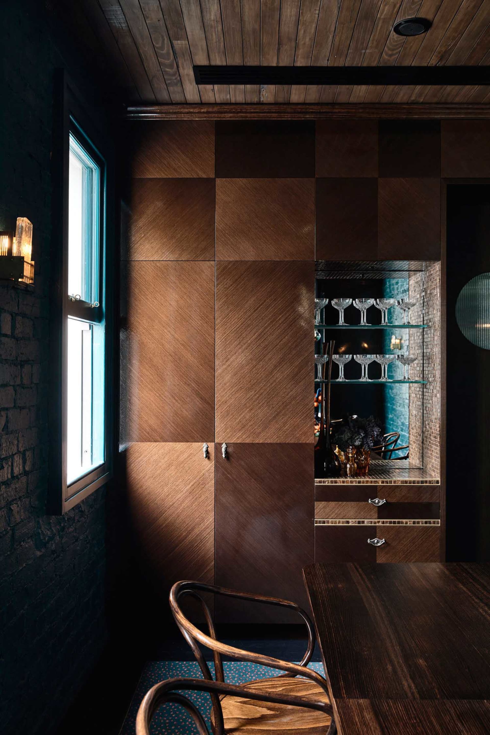 Modern kitchen with wooden cabinets, a wine rack, and bottles on the countertop, lit by natural sunlight
