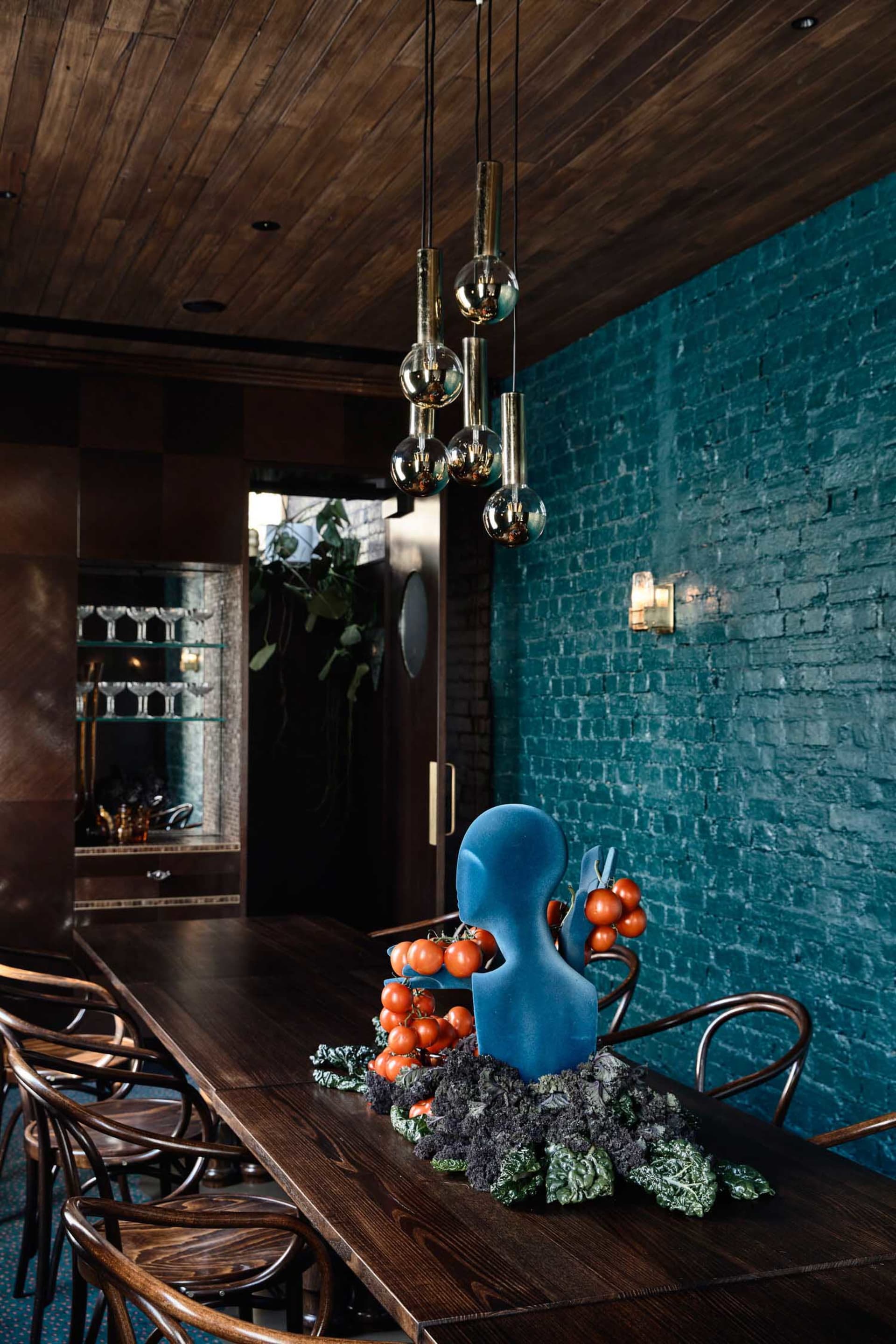 Warm and inviting dining area with a wooden table, chairs, wine glasses, and fresh fruits, set against a brick-patterned wall