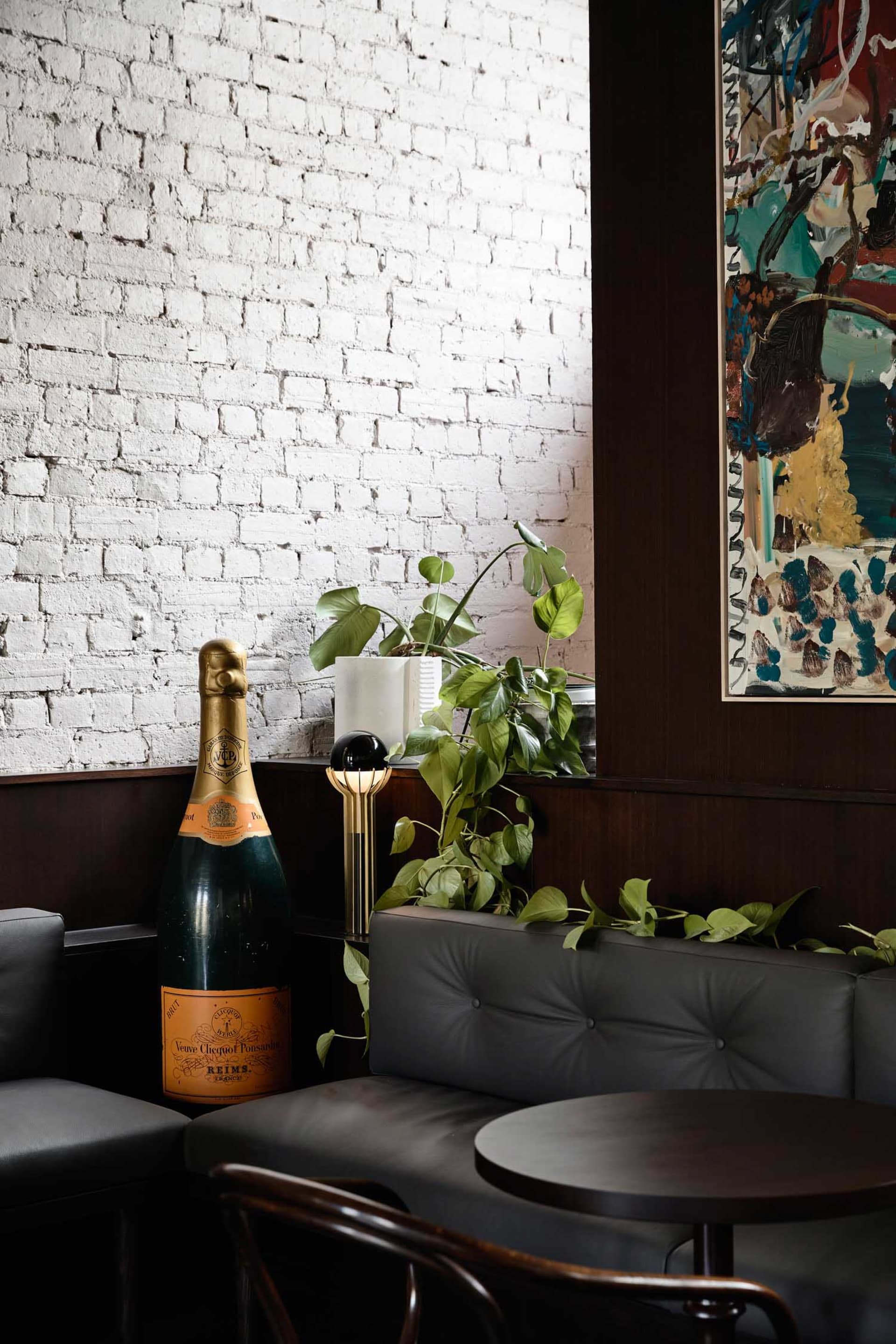 A living area with a couch, chair, and dining table, featuring brick walls, potted plants, and a bottle of wine, creating a warm and inviting atmosphere