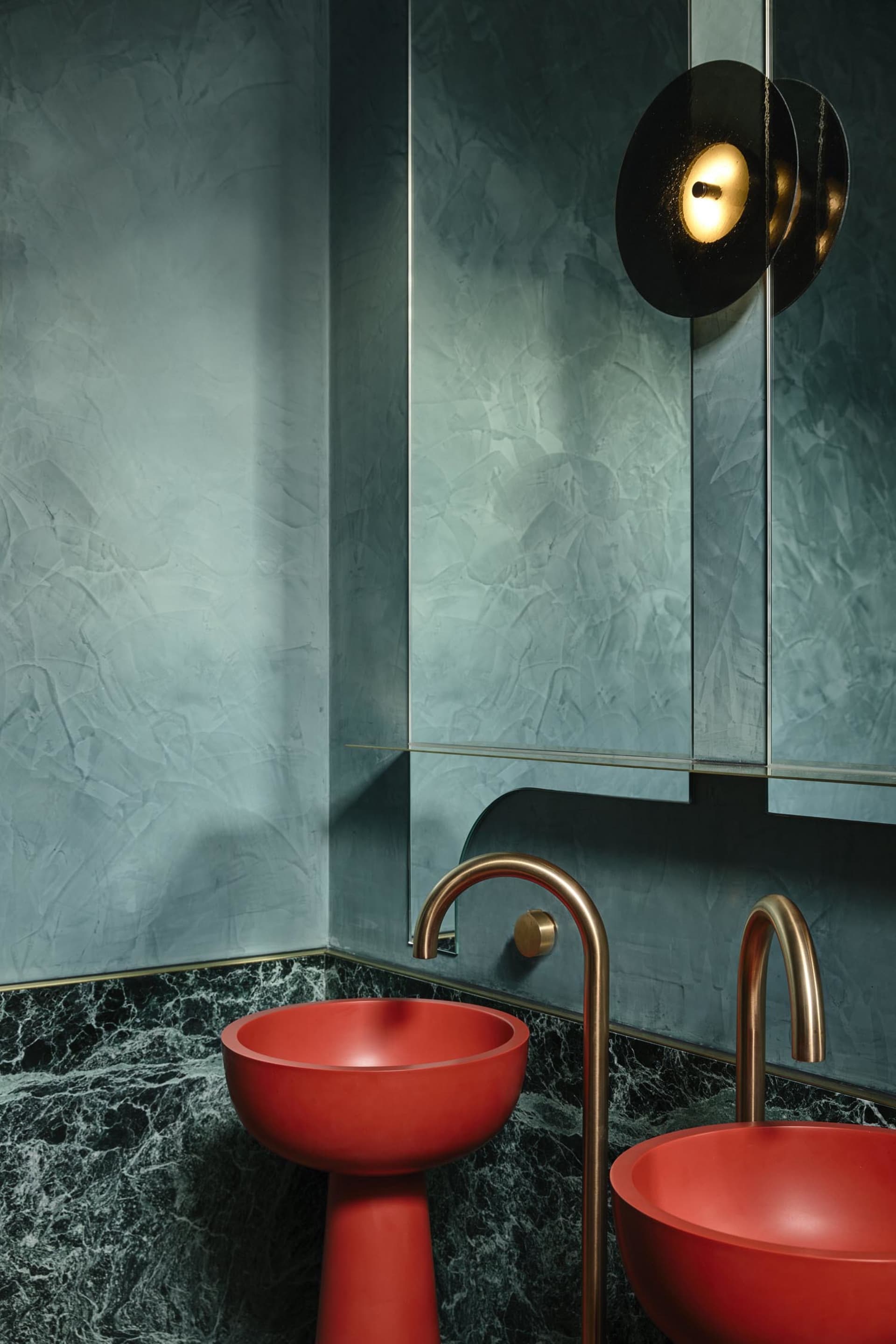 Bathroom with a red bowl sink on a marble countertop, blue walls, and a gold faucet, creating an elegant and luxurious atmosphere