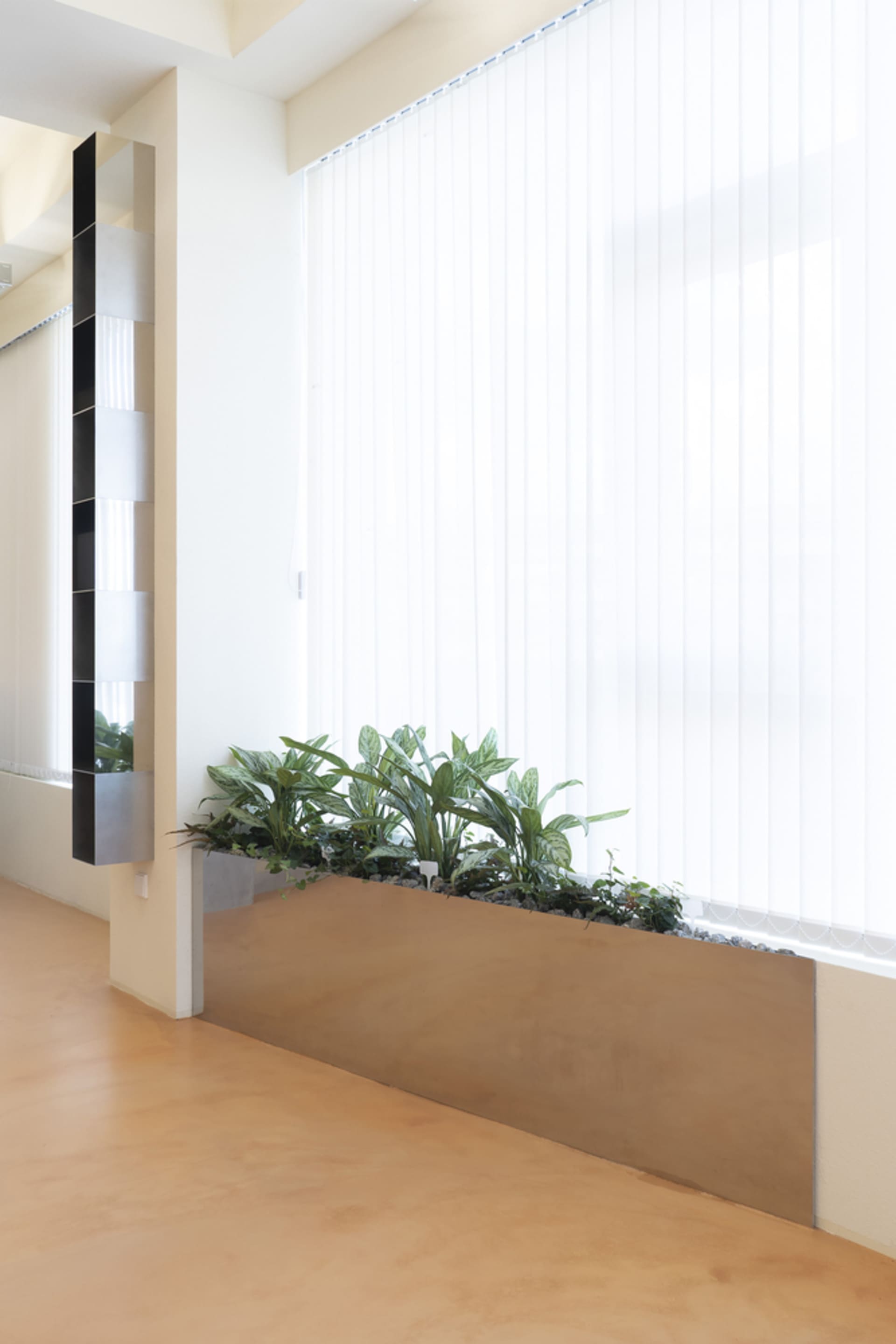 A calm and inviting indoor space with a large window, white curtains, and several potted plants adding a touch of greenery