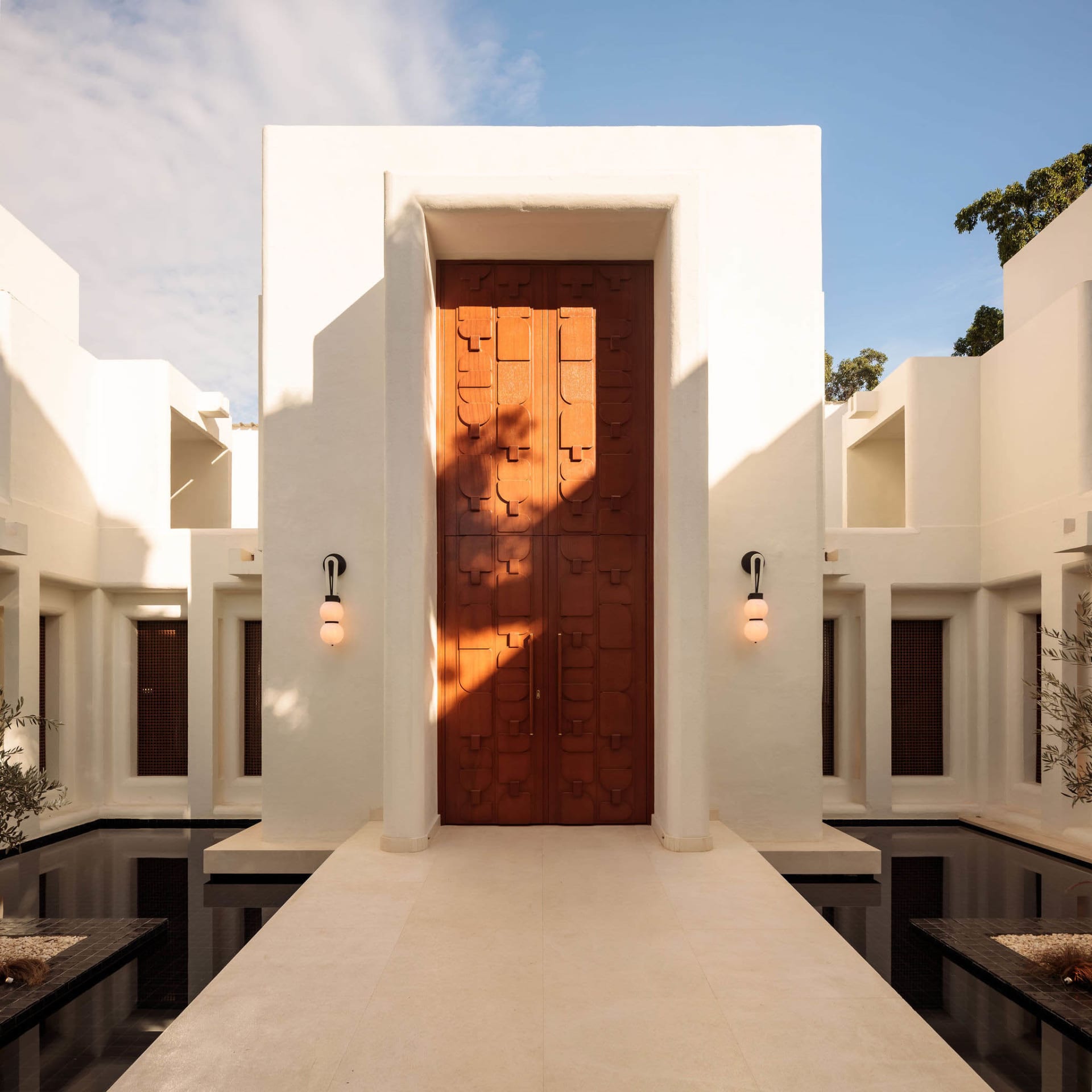 A white building with a large wooden door and a patio area, set in a daytime scene with natural light