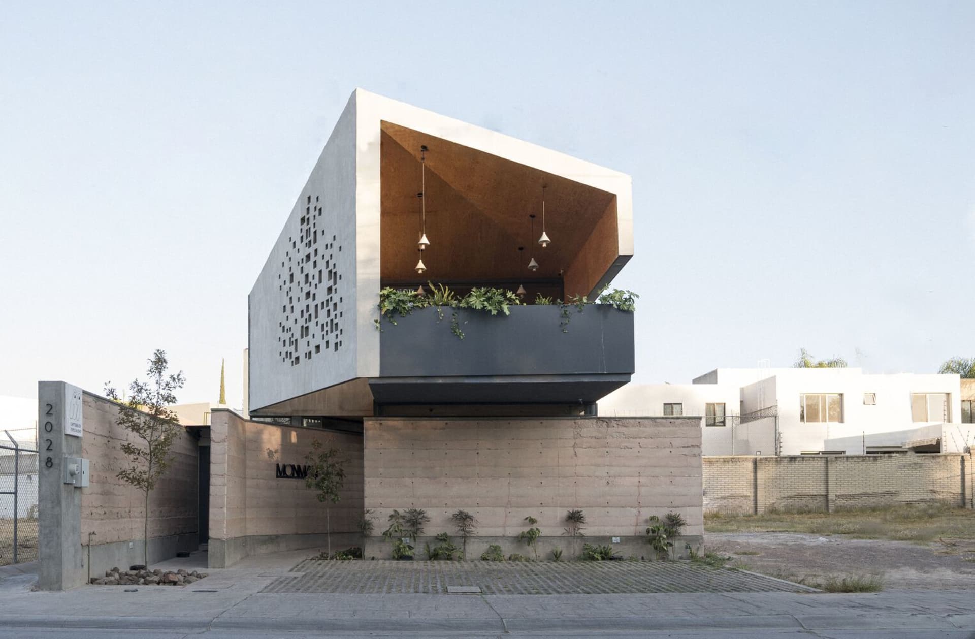 A modern building with a concrete facade, featuring a large overhang and potted plants around the structure, conveying a sense of urban design and contemporary architecture