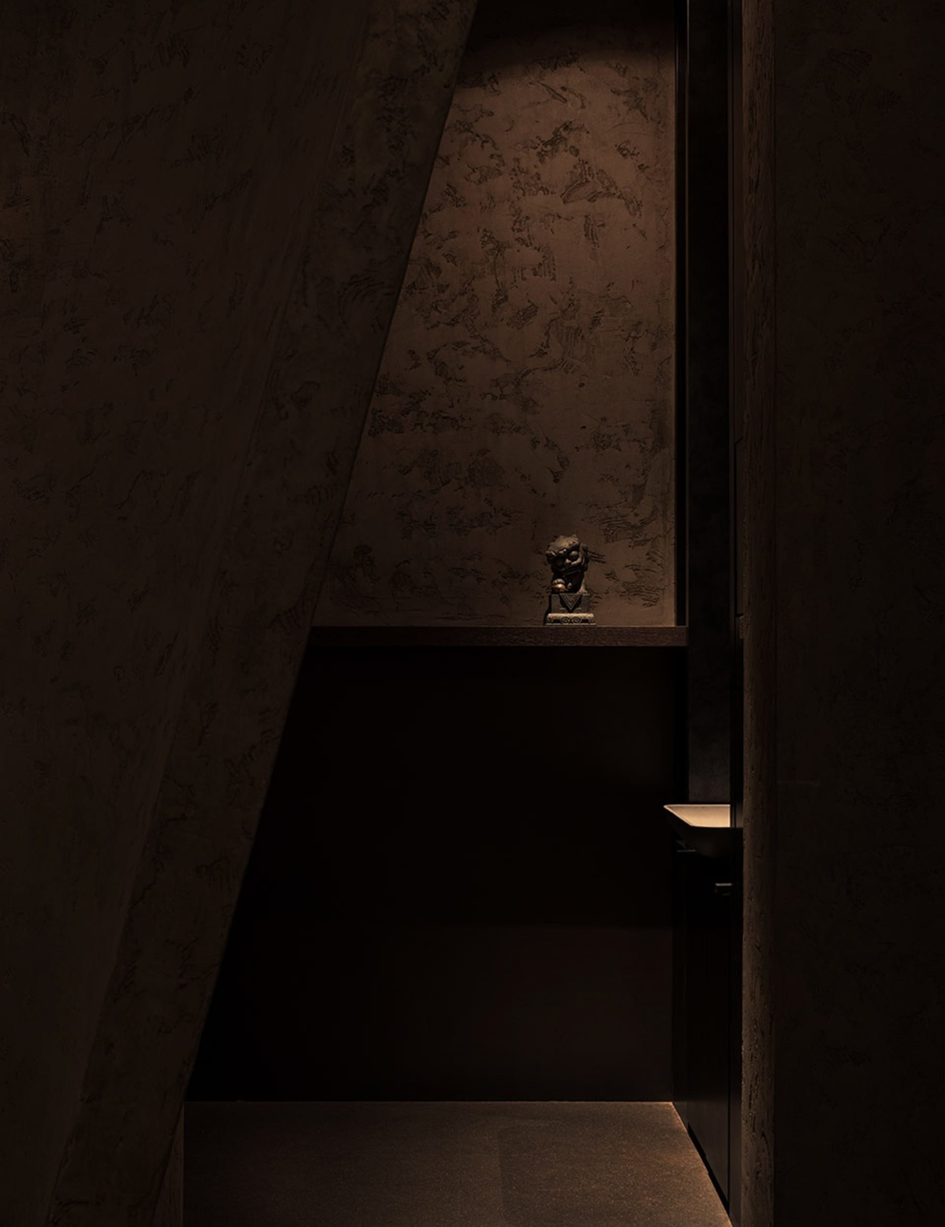 Dark hallway with a stone wall, a wooden door, and two statues on display