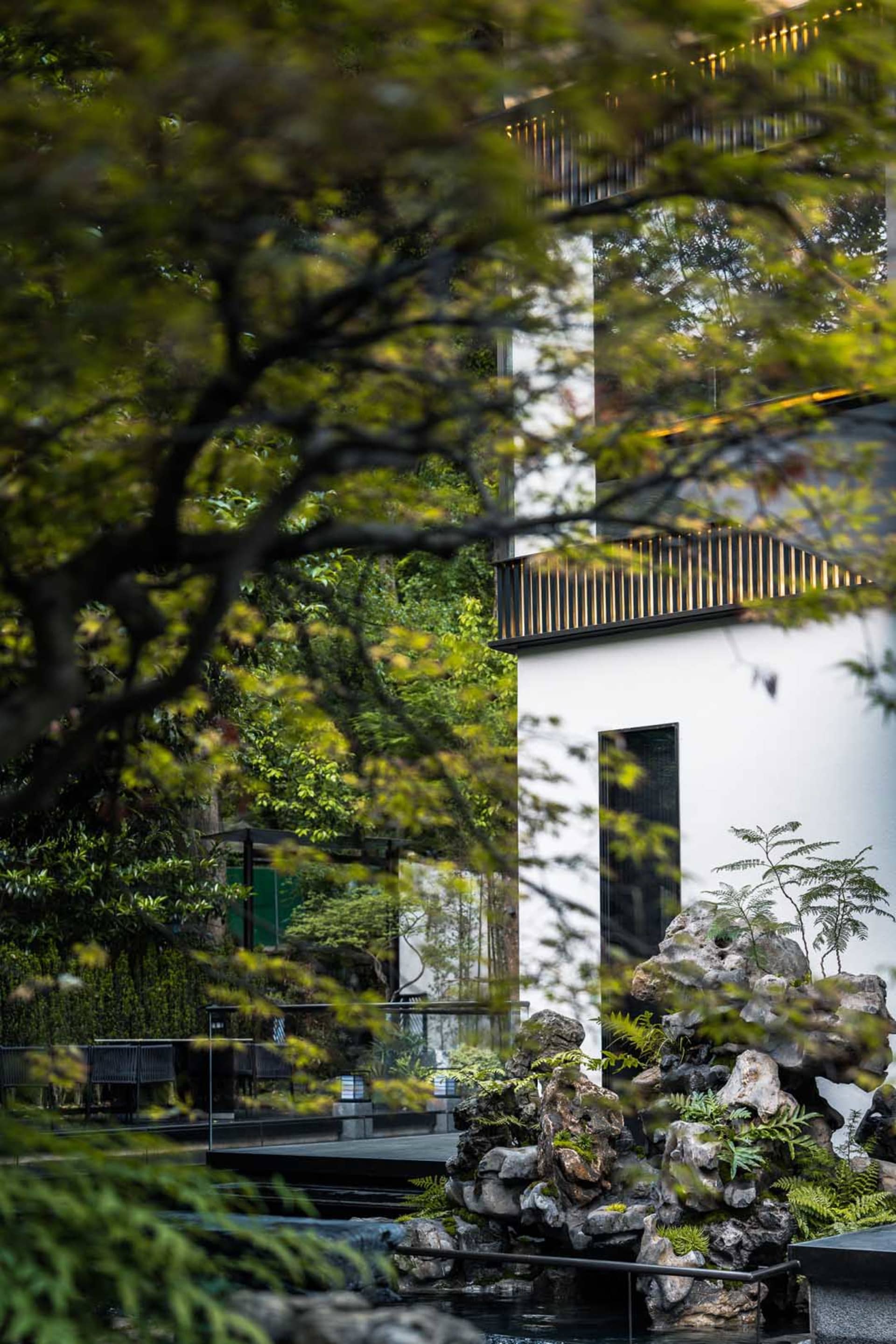 A serene Asian-style house with a white exterior, surrounded by trees and greenery, featuring a large window and a blend of traditional and modern architectural styles