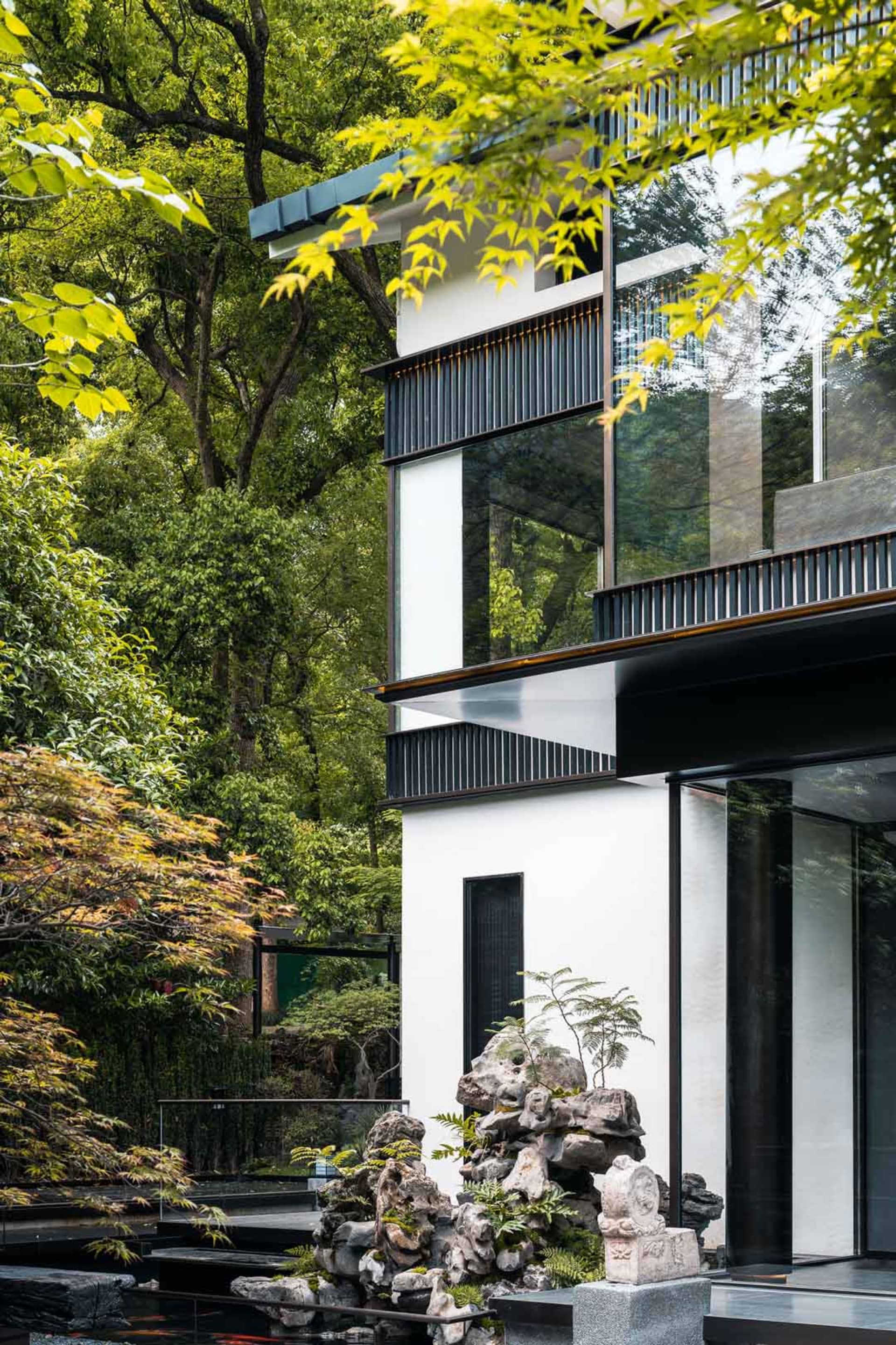 A modern house with a large white exterior, surrounded by trees, featuring black accents and multiple windows for natural light, creating a calm and serene atmosphere