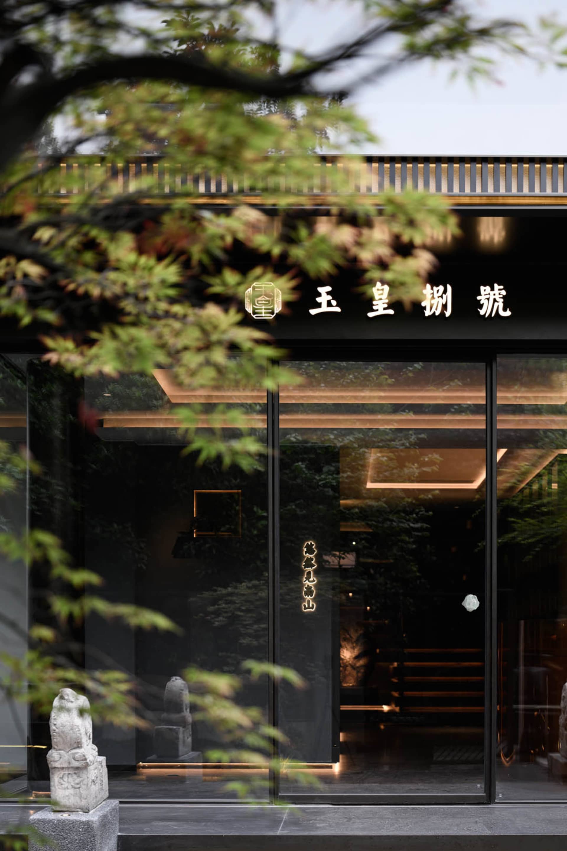 一座傳統亞洲建築，黑色門廊通往燈光明亮的走廊，展示兩尊雕塑