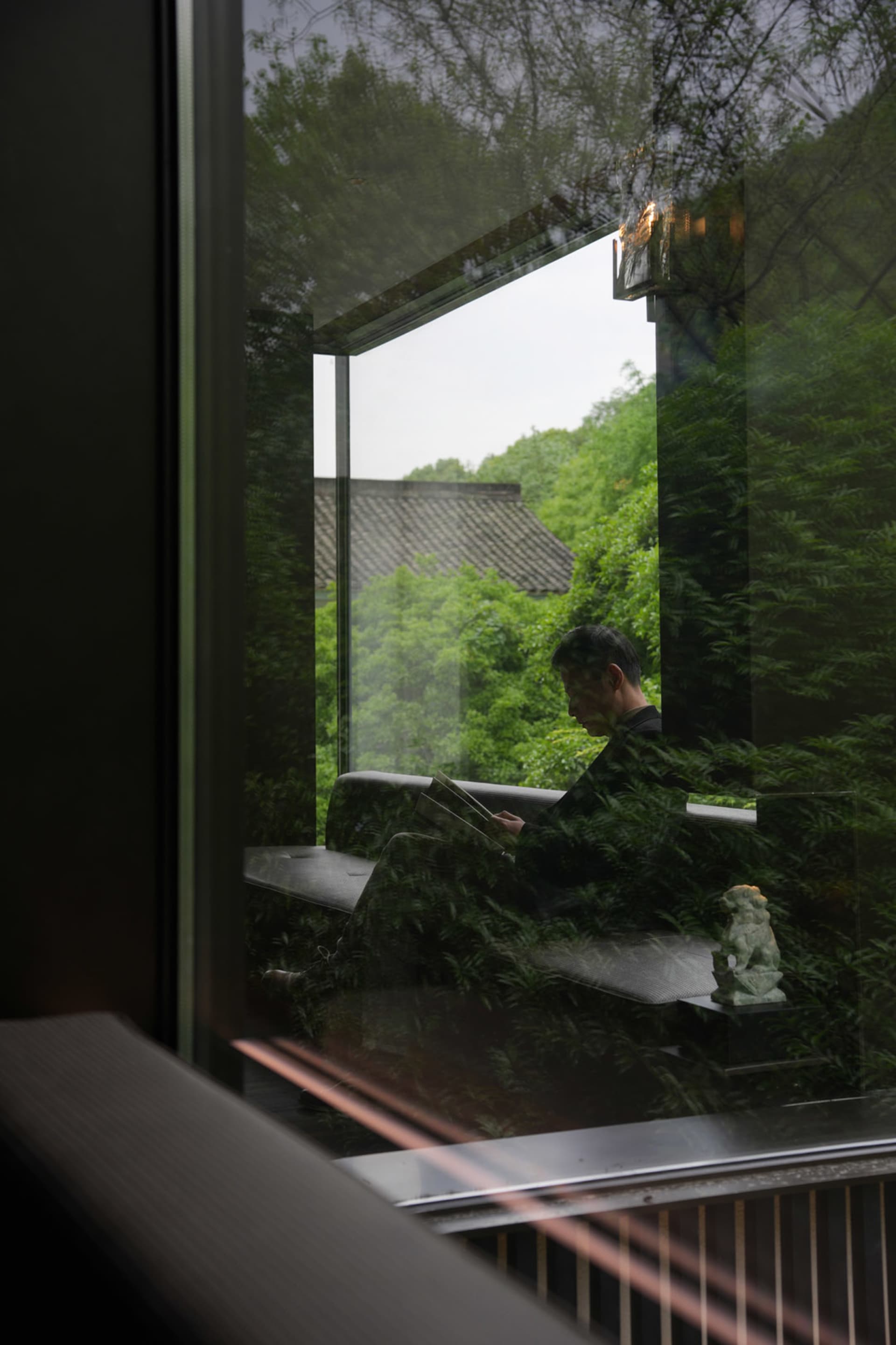 一名男子坐在寧靜客廳的長椅上，周圍環繞盆栽與窗外自然光線