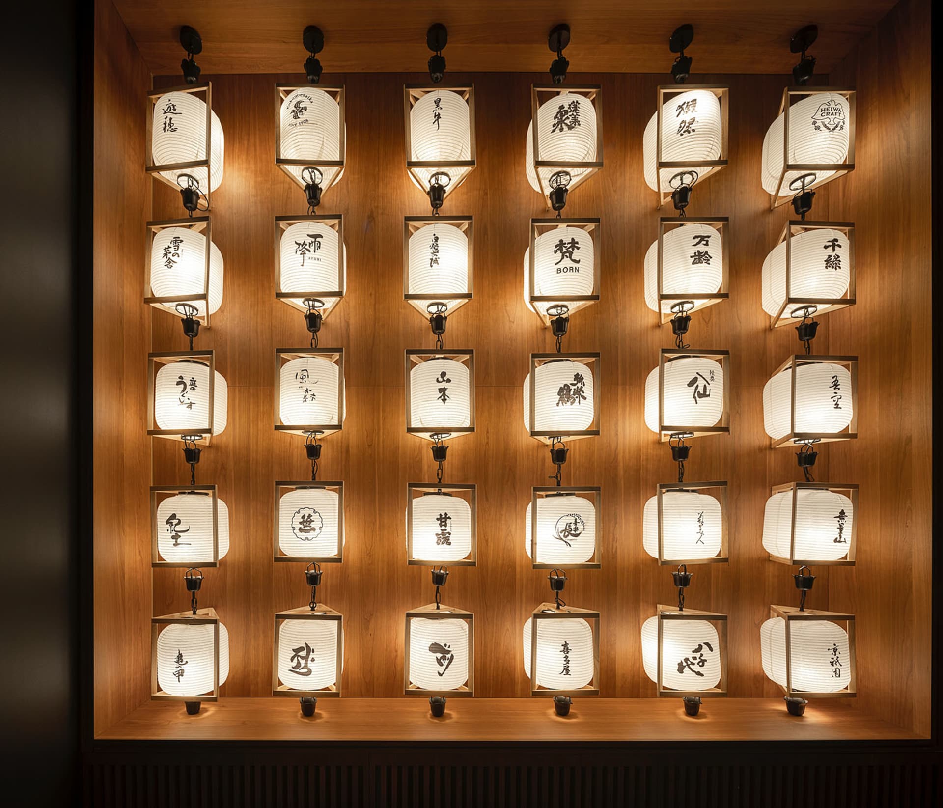 A museum-style display of Asian characters on wooden panels, illuminated by lights, arranged in rows for a visually appealing presentation