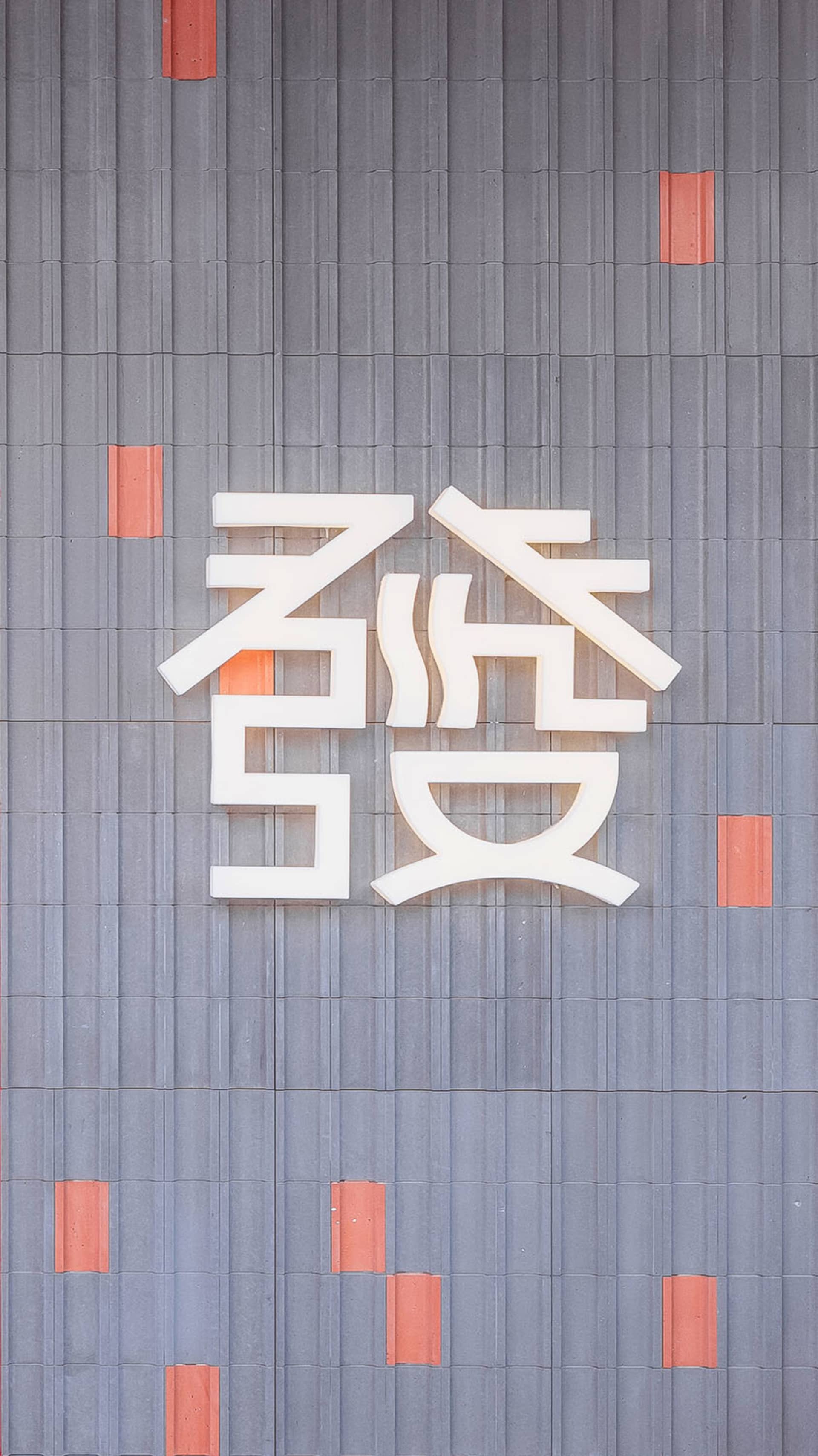 一座當代亞洲建築，擁有大型白色招牌，融入現代設計與橙色點綴，背後是都市景觀