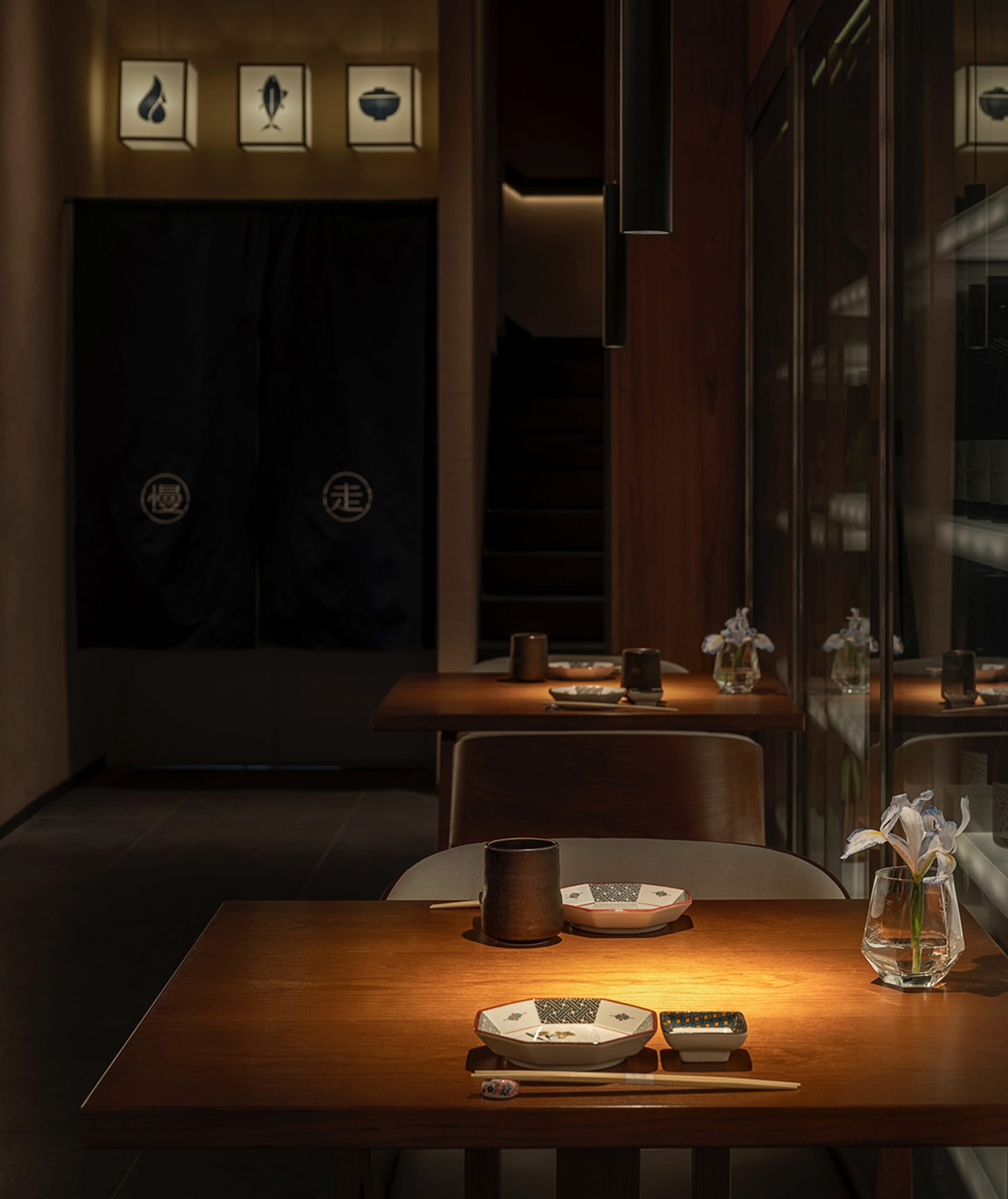 Elegant Asian restaurant interior with wooden tables, chairs, and glass elements, featuring a mix of modern and warm ambiance, with vases adding a touch of sophistication