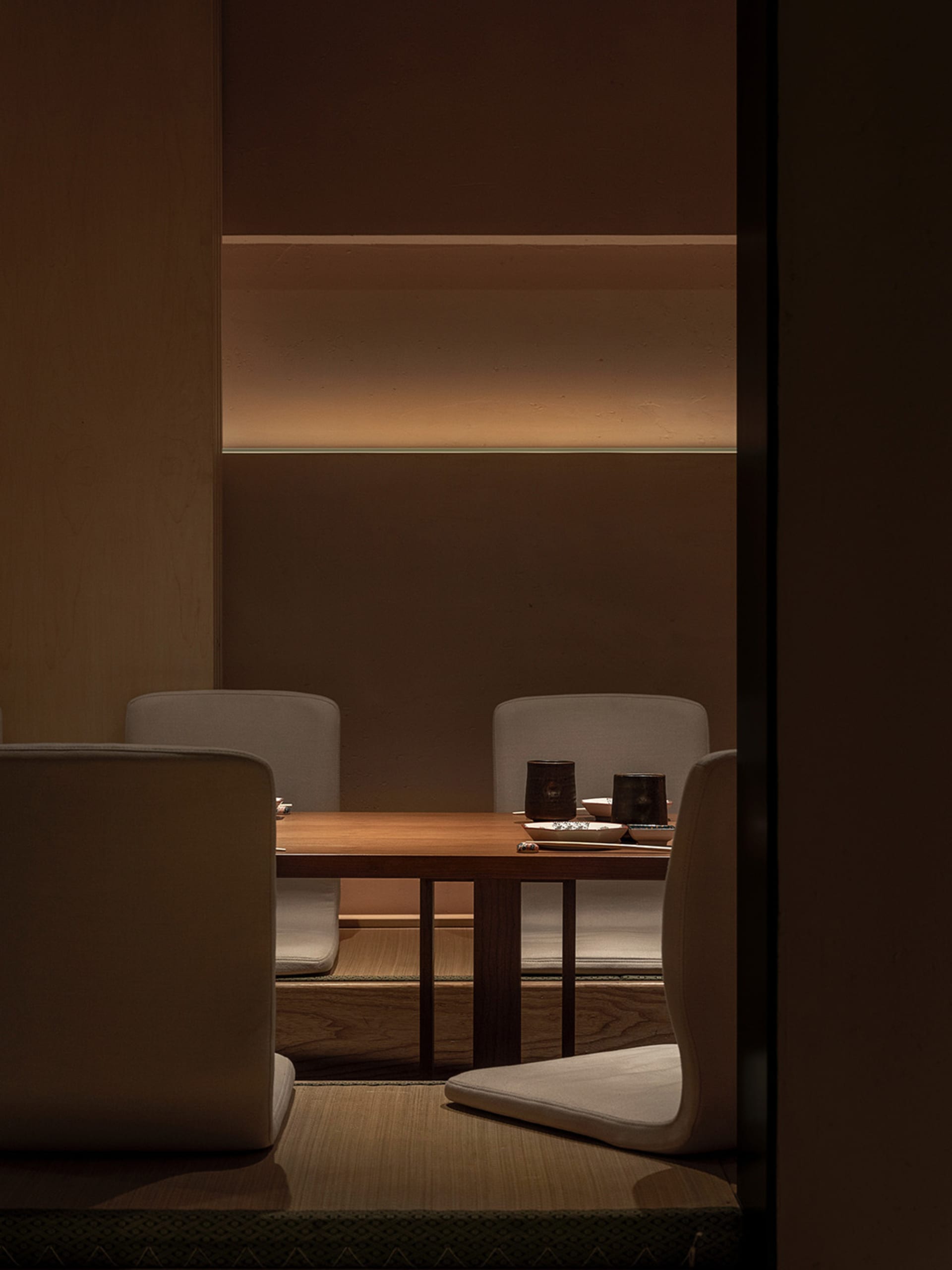 Empty dining area with three white leather chairs around a wooden table near a brown-tinted wall
