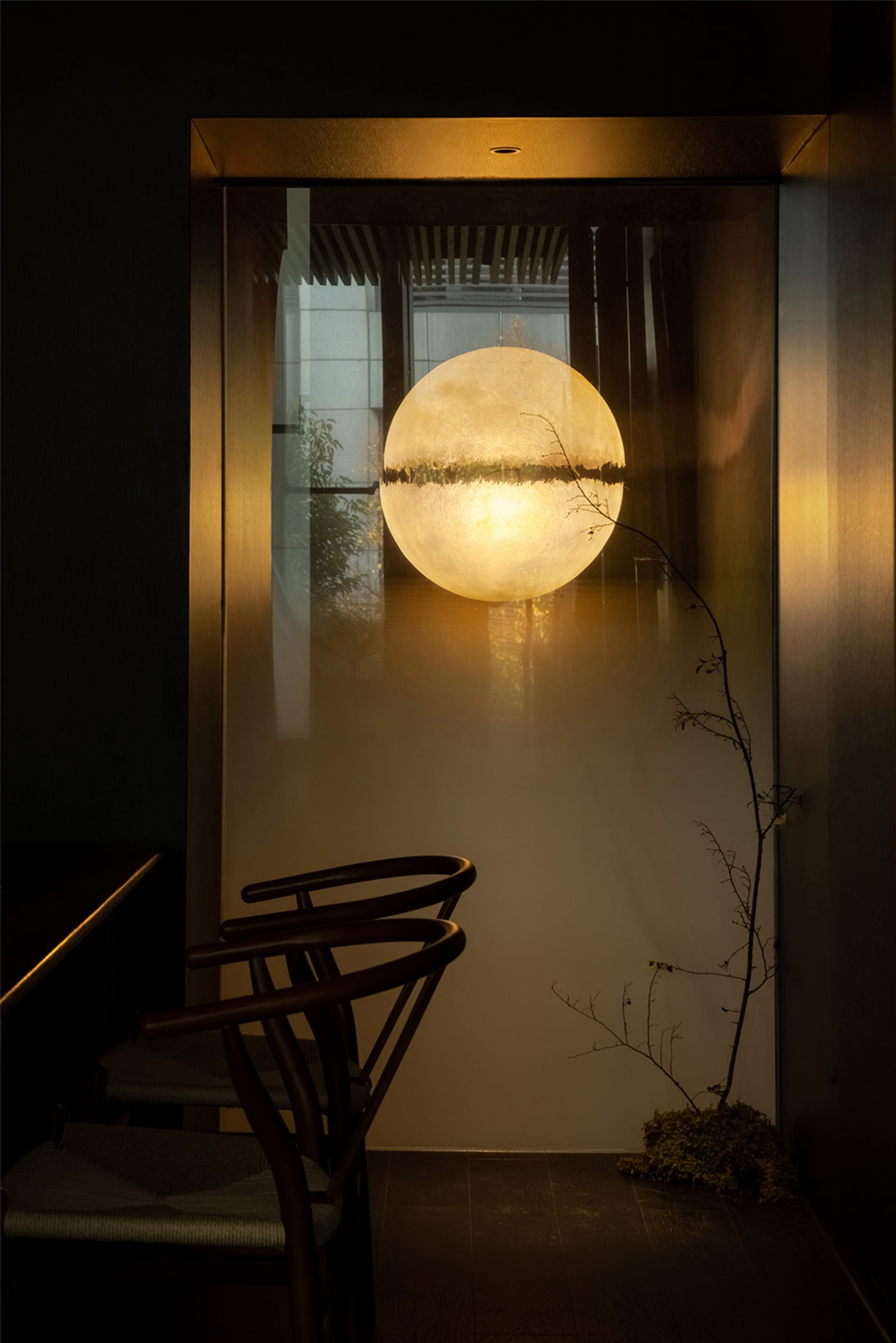 A dimly lit room with a chair in front of a window featuring a reflection of a round object, creating an interesting visual effect