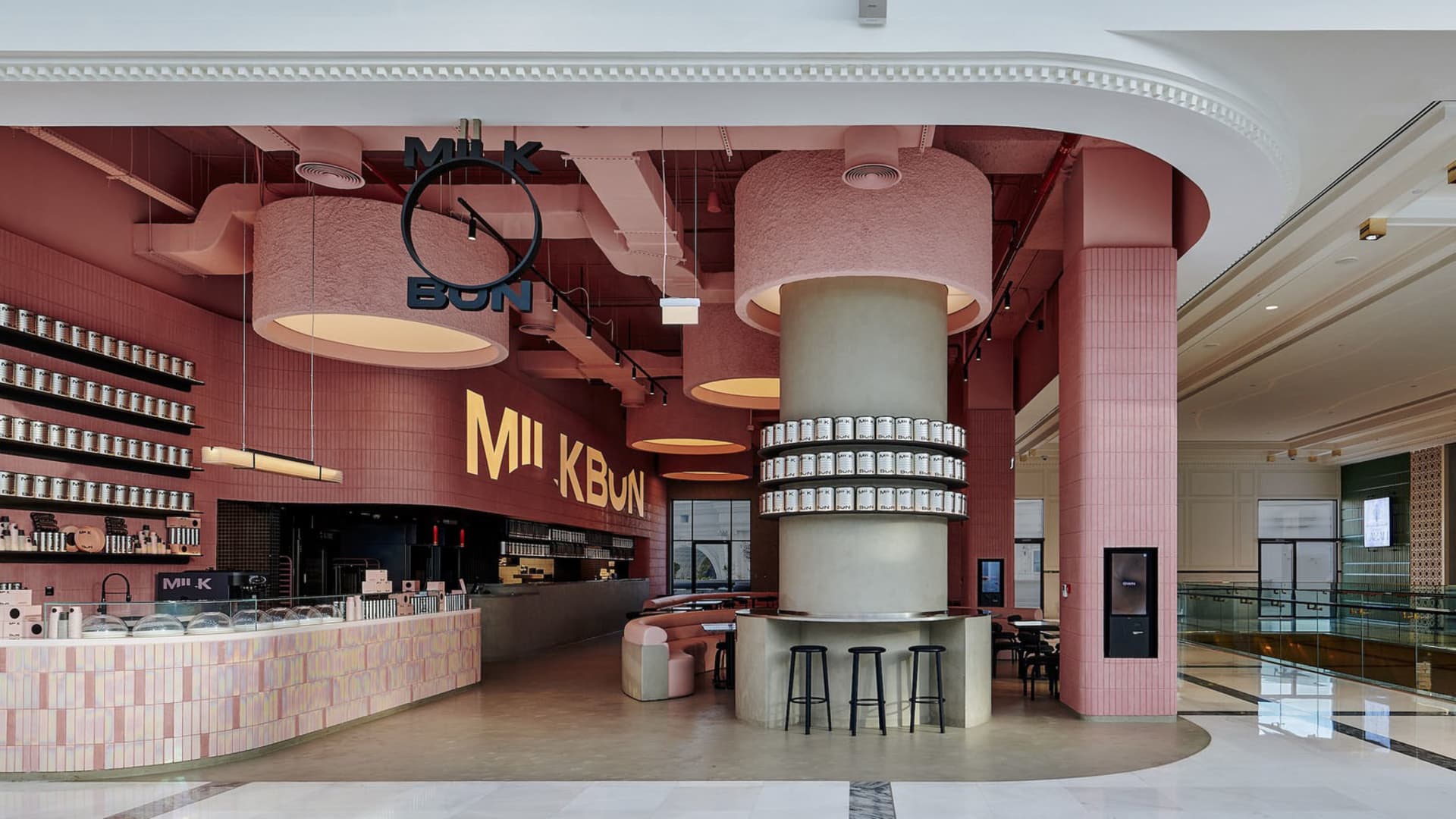 Inviting restaurant interior with a pink and white color scheme, featuring a bar, dining table, and various seating options, with bottles and a welcoming atmosphere