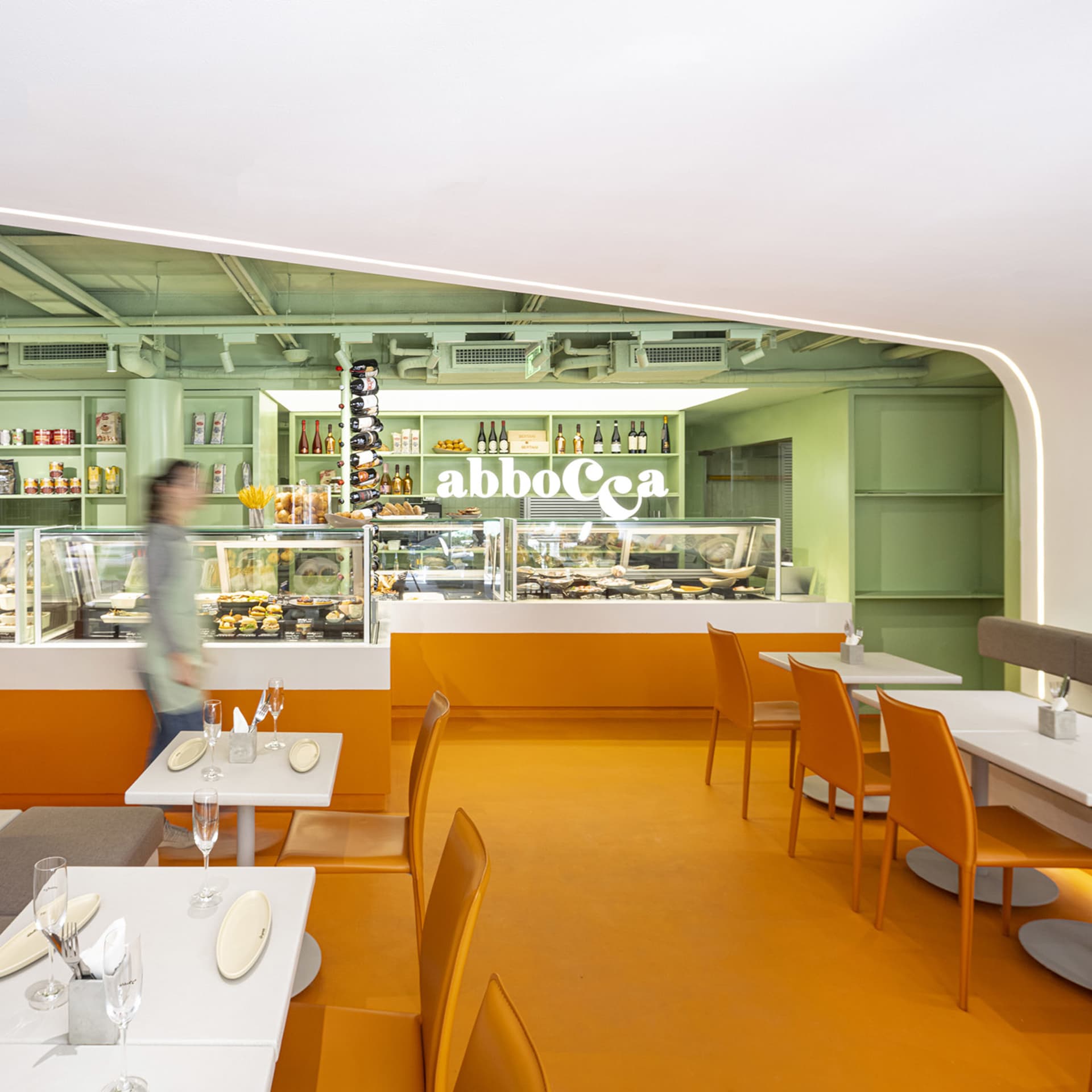 A warm and inviting dining area with orange walls, wooden tables and chairs, and wine glasses on the tables
