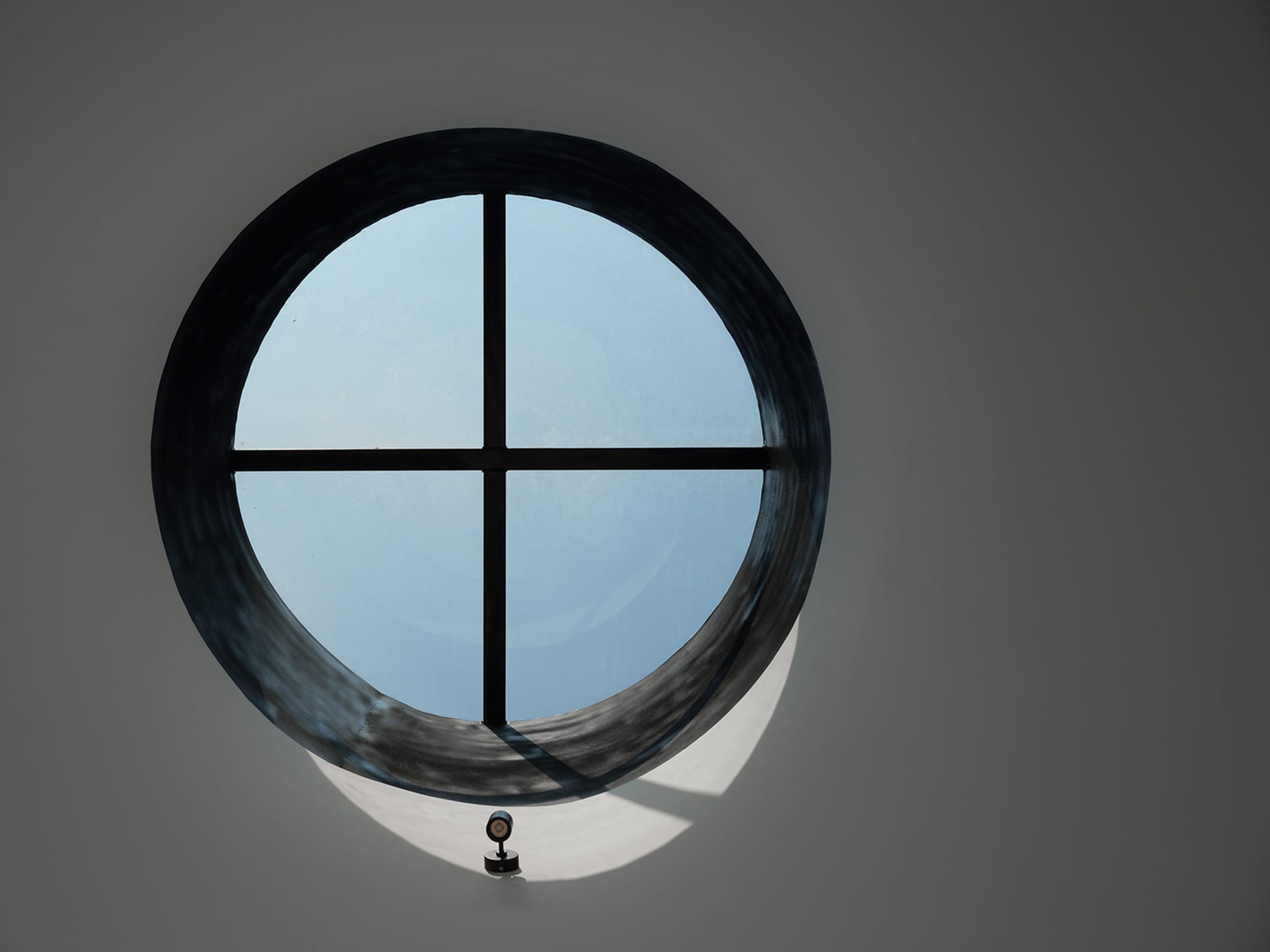 A dimly lit scene with a round window featuring a black frame and a small lamp inside