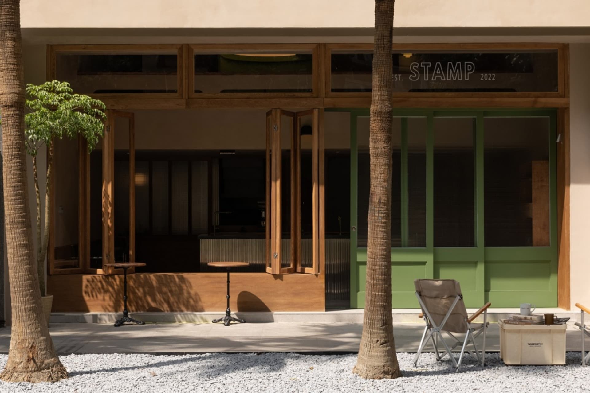 A relaxed outdoor dining area with a green door, palm tree, and a few chairs and a table