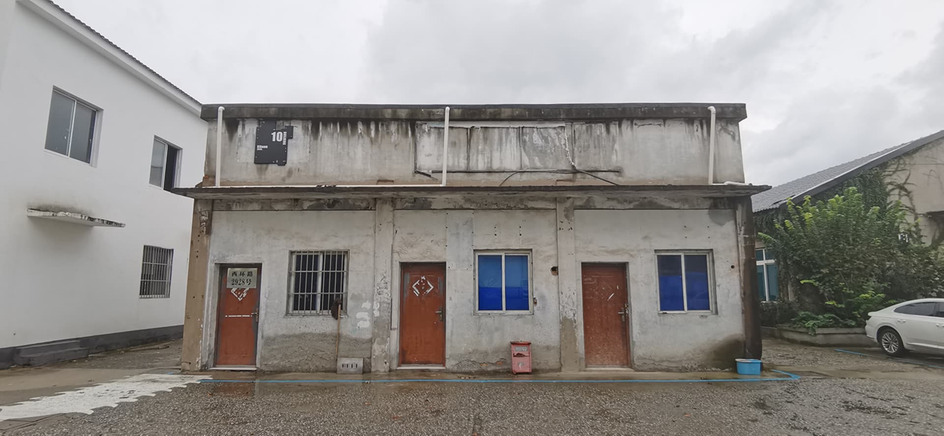 Aged building with a weathered concrete facade, featuring two doors and two windows, with a neglected appearance