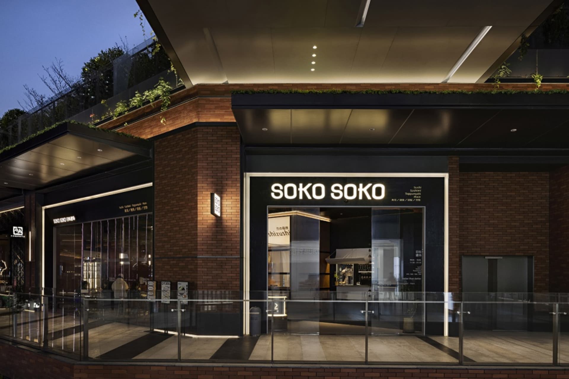 A modern building with a brick facade and black and white color scheme, surrounded by potted plants and illuminated at night