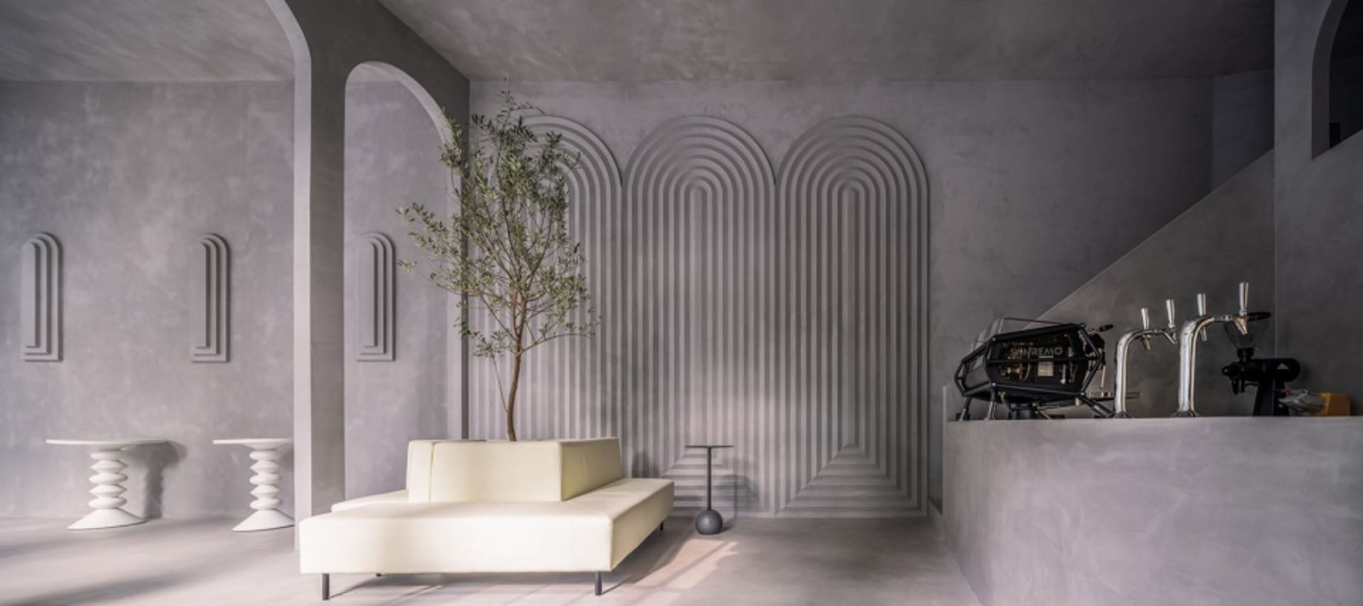 Modern living area with a couch, chair, and dining table, surrounded by a unique spiral-patterned wall and two potted plants, with a warm and inviting atmosphere