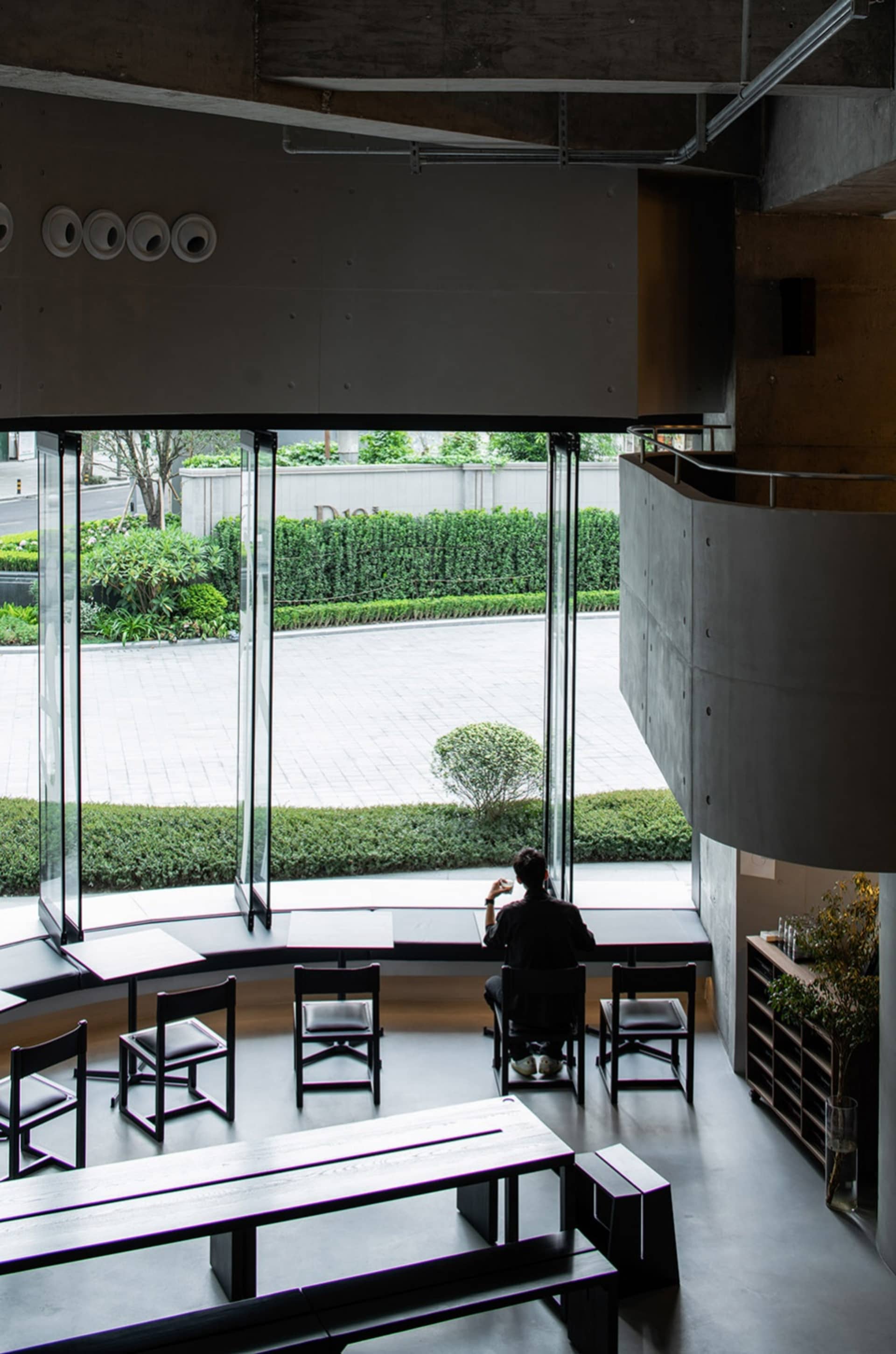 Calm and inviting living-dining space with natural light, wood, and glass, featuring a man sitting at a desk in front of a window