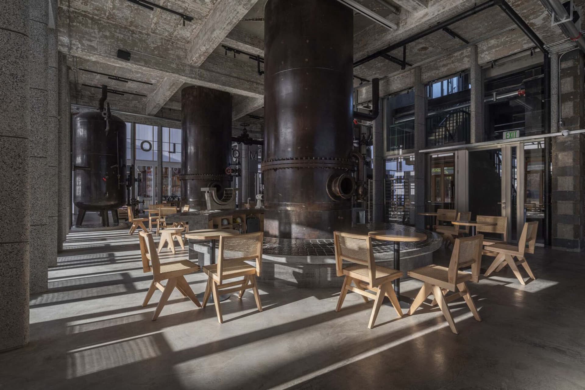 Industrial cafe with cylindrical tanks, chairs, and dining tables, surrounded by benches for social seating