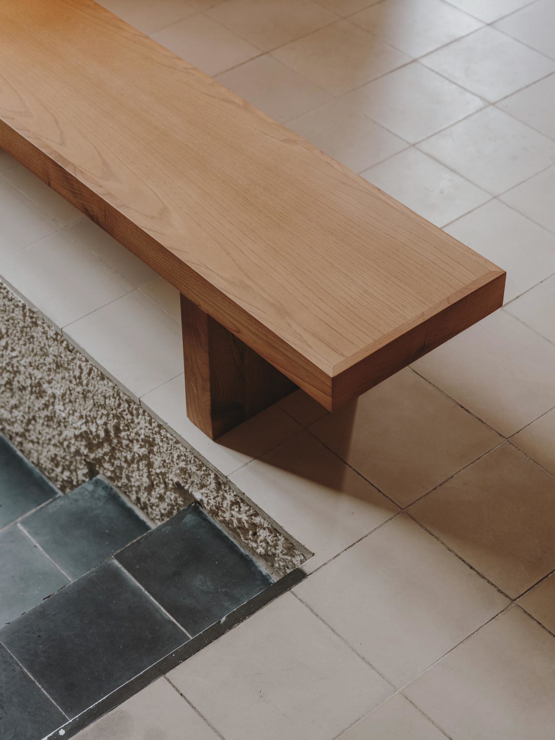 A calm and inviting room with a wooden bench on a tile floor, featuring a simple design and a patterned tile layout