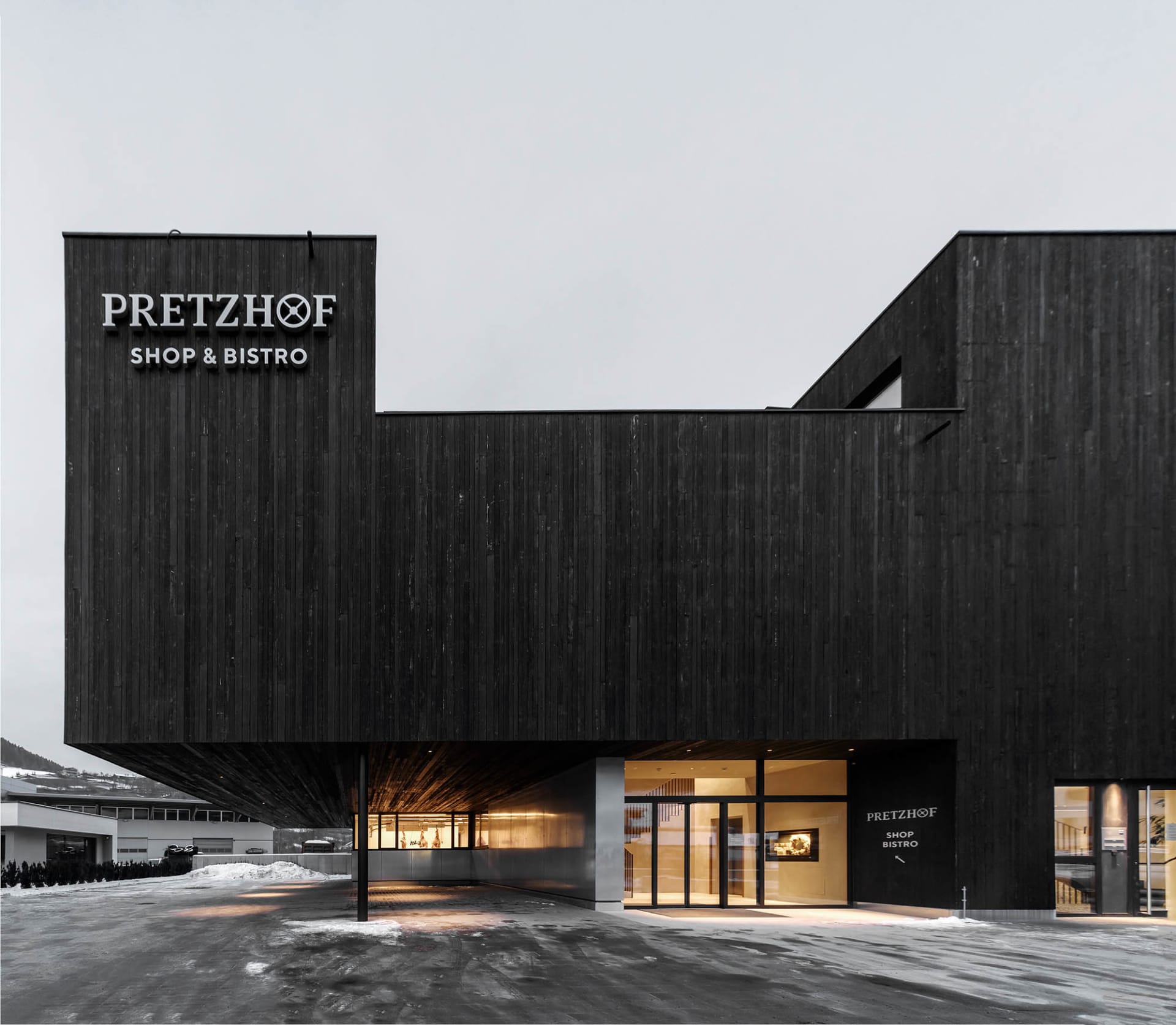 Modern building exterior with a black facade, wooden structure, and two entrances