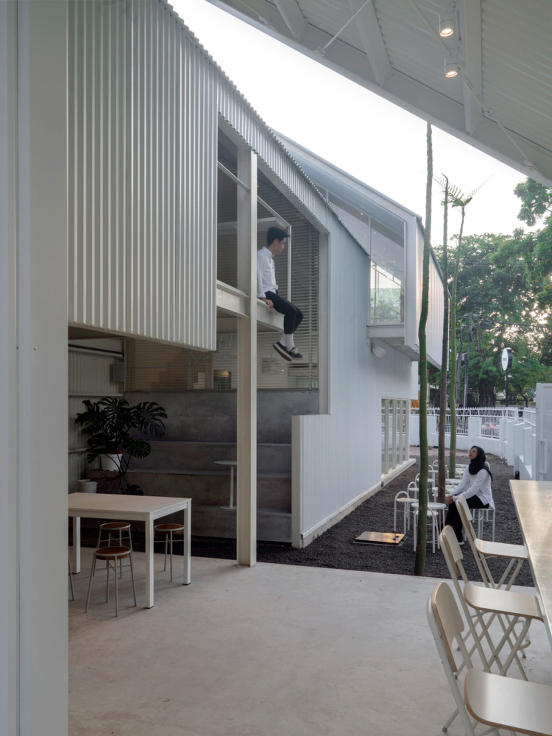 A modern living-dining space with white walls, wooden furniture, and a relaxed atmosphere, featuring a person sitting on a chair