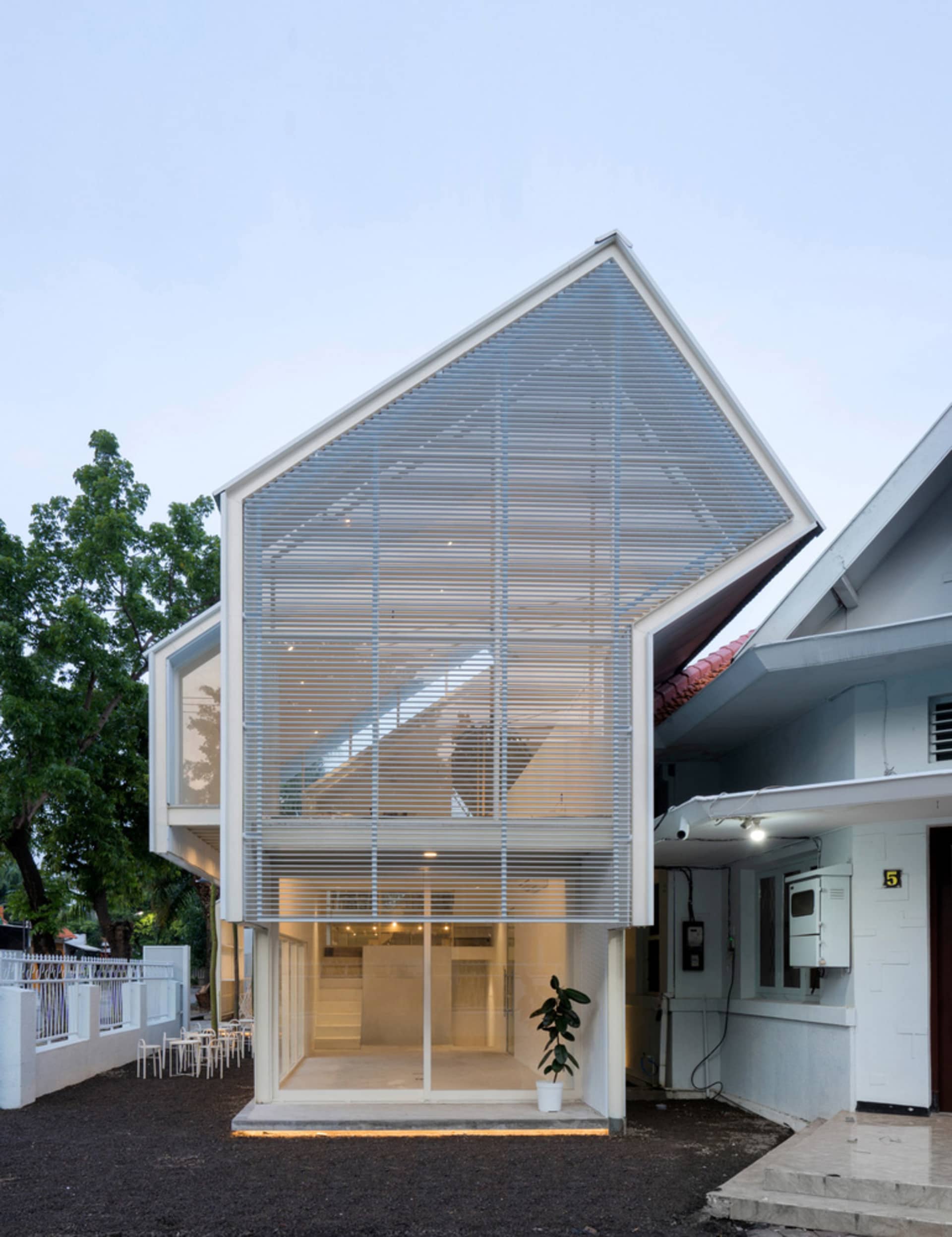 Modern house with a large glass wall, minimalist design, and outdoor seating area with chairs